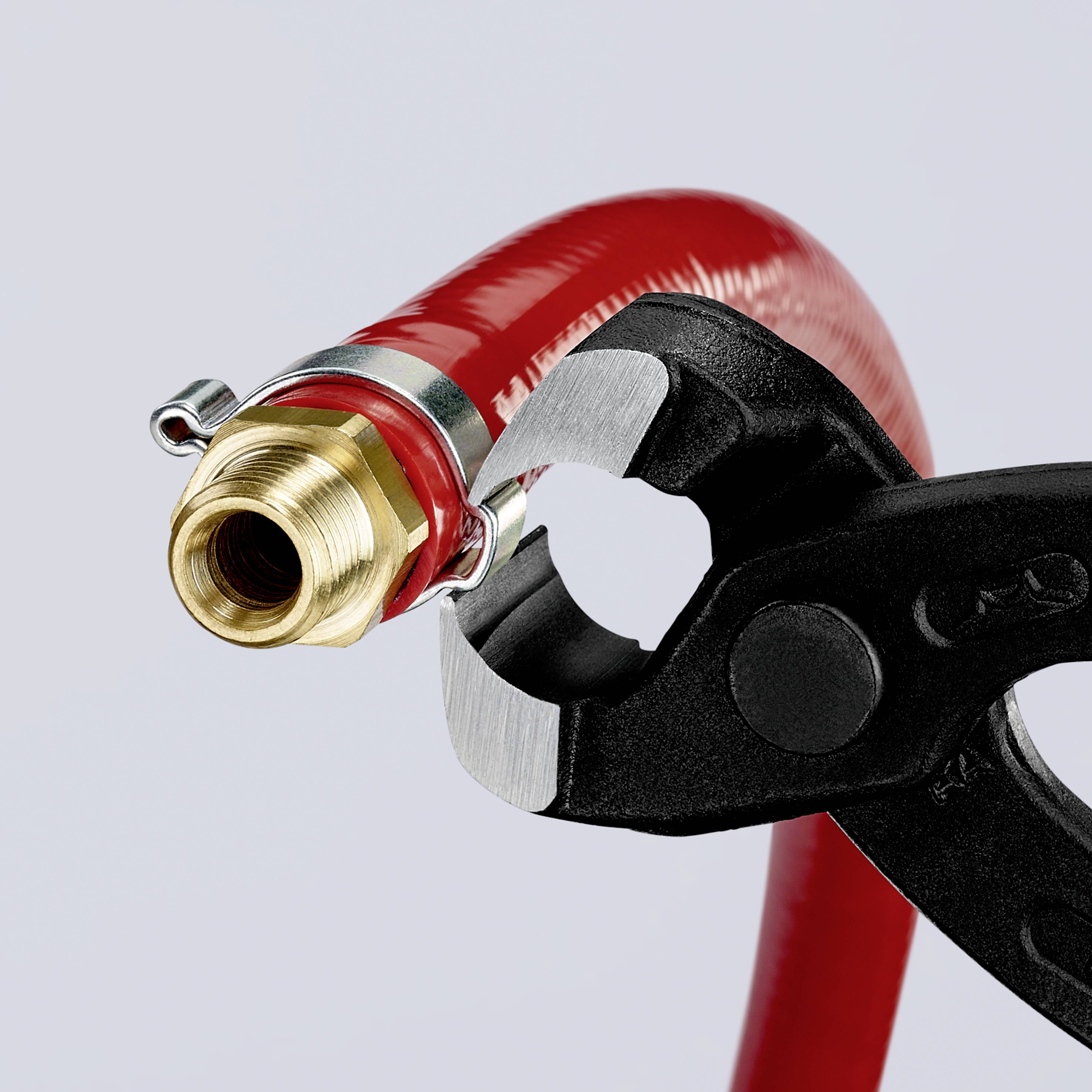 Eine Zange hält eine rote Schlaucharmatur mit einem Metallanschluss, der Anschein nach wird eine Reparatur oder Montage durchgeführt.