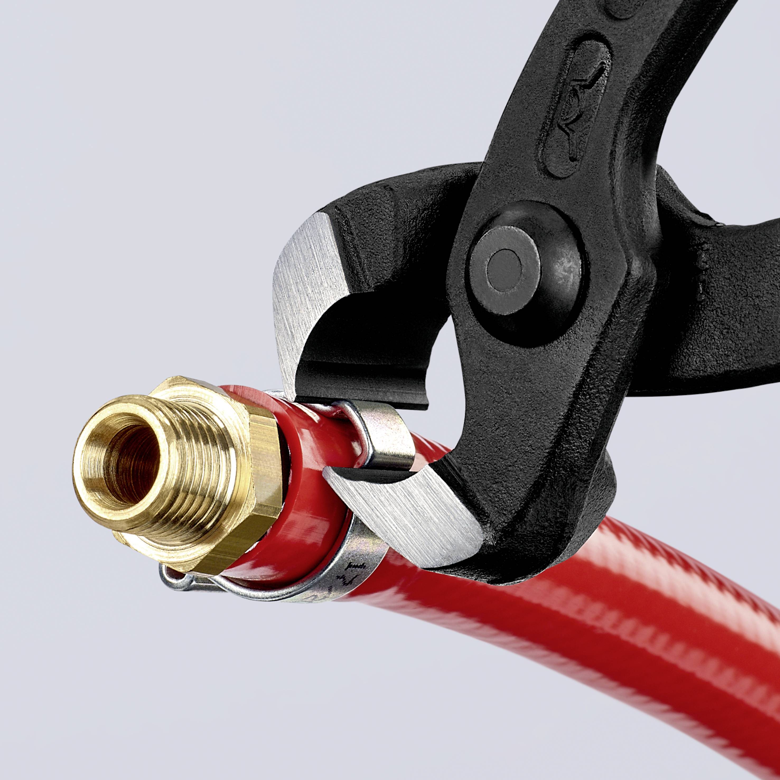 Eine Zange hält ein rot lackiertes, metallisches Objekt, möglicherweise Teil einer hydraulischen oder wasserführenden Verbindung.