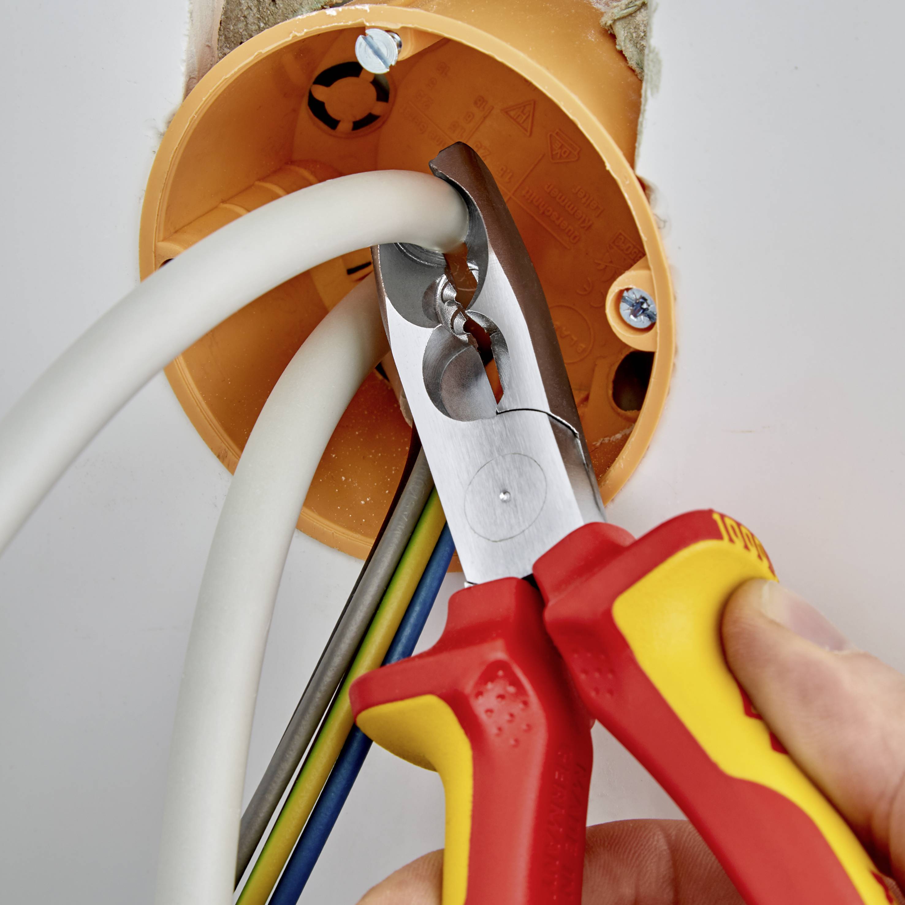 Eine Person zieht mit einem roten Seitenschneider elektrische Kabel durch ein orangefarbenes Rohr.