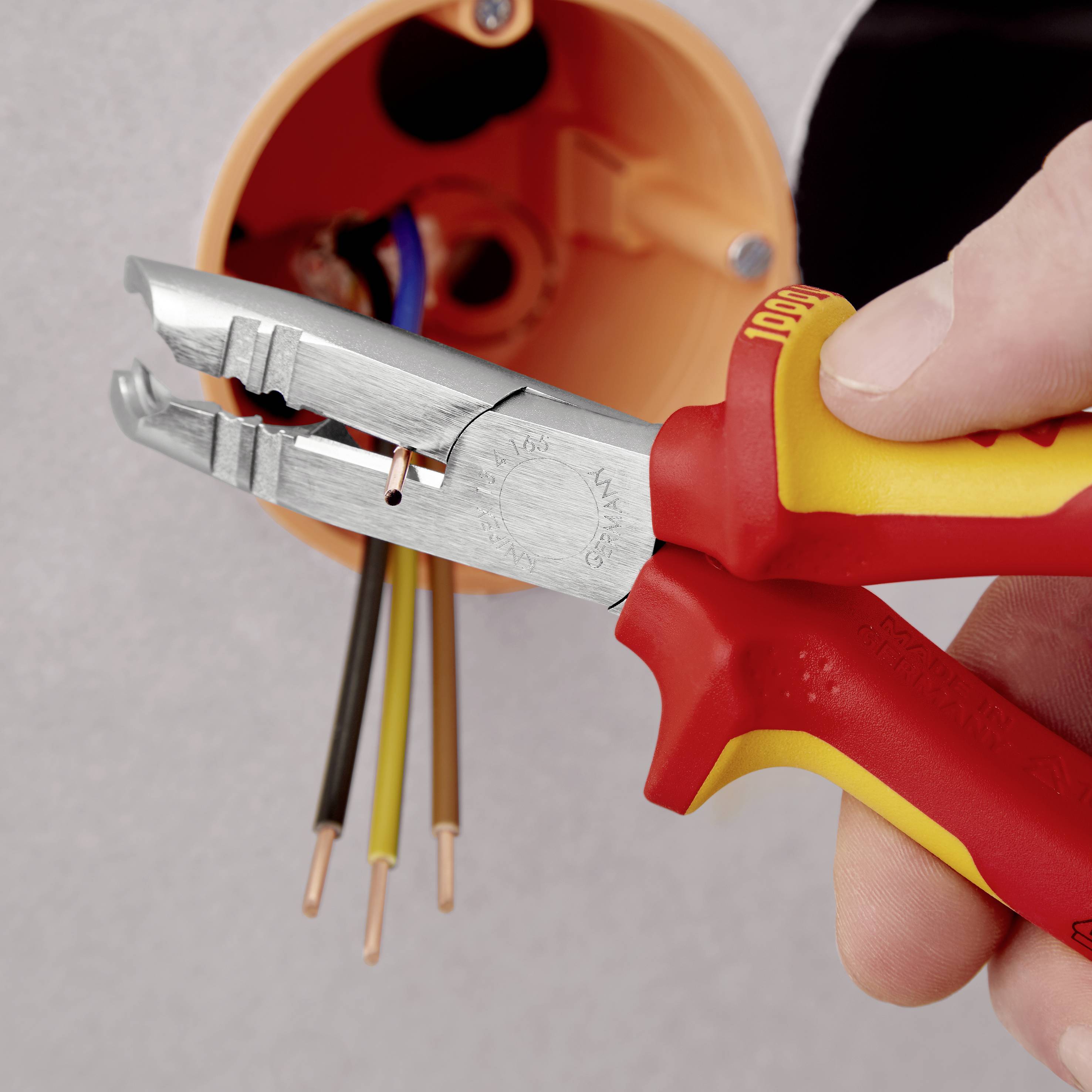 Eine Hand benutzt eine Abisolierzange, um die Isolierung von elektrischen Kabeln in einer Steckdose zu entfernen.