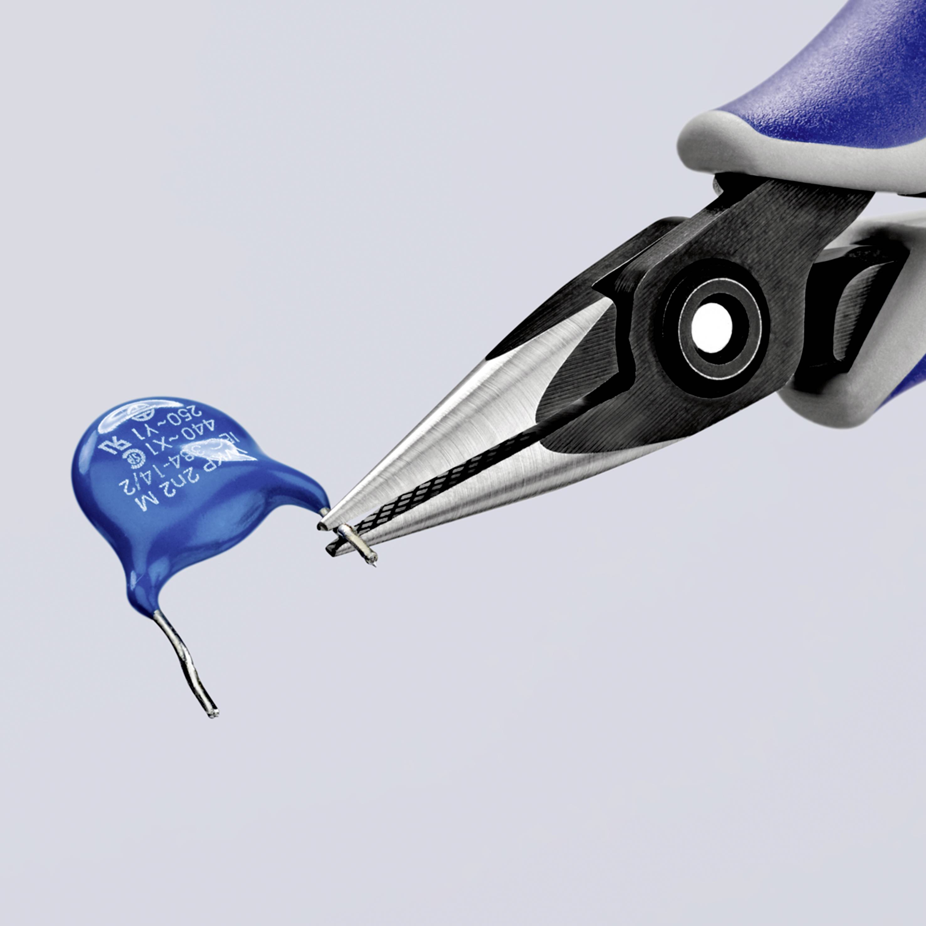 Eine blaue Zange hält einen blauen Kondensator mit Beschriftung, zeigt einen kleinen elektronischen Bauteilreparaturvorgang.