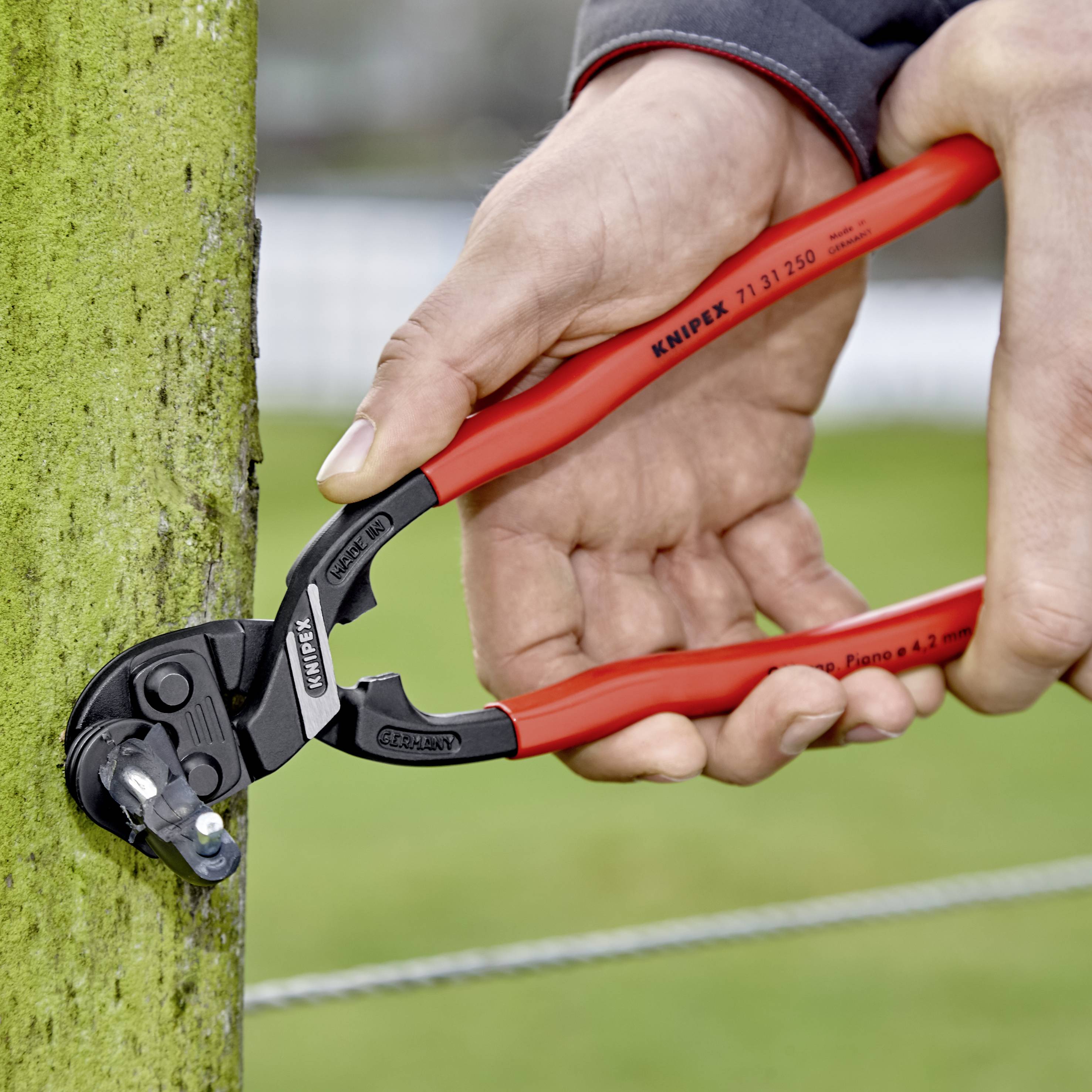 Eine Person benutzt eine rote Knipex-Kabelschere, um ein grünes Kabel in einem Außenbereich zu schneiden.
