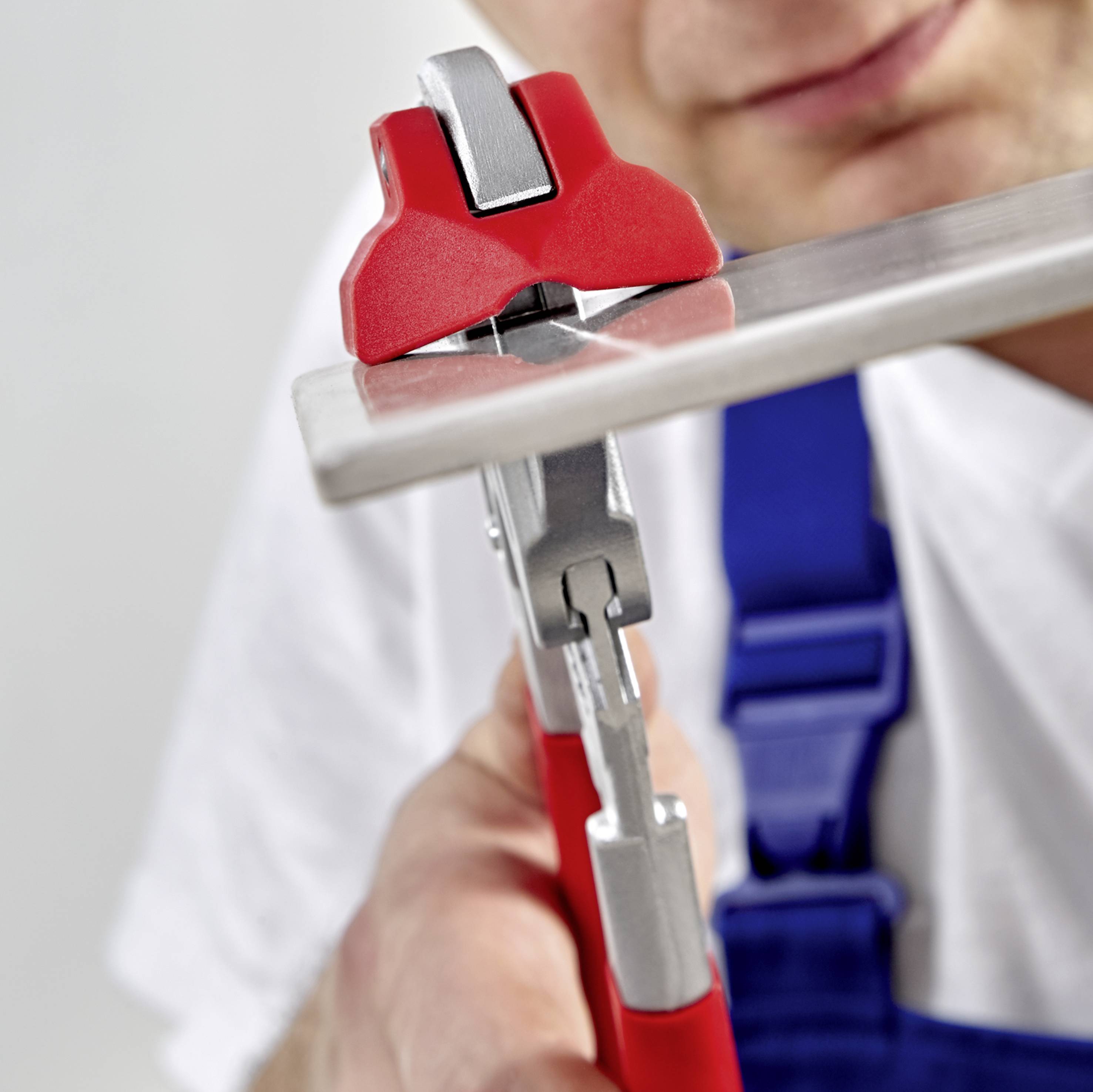 Ein Klempner benutzt eine Rohrzange mit rotem Griff, um ein Metallrohr zu drehen. Der Fokus liegt auf der Arbeitshandlung.