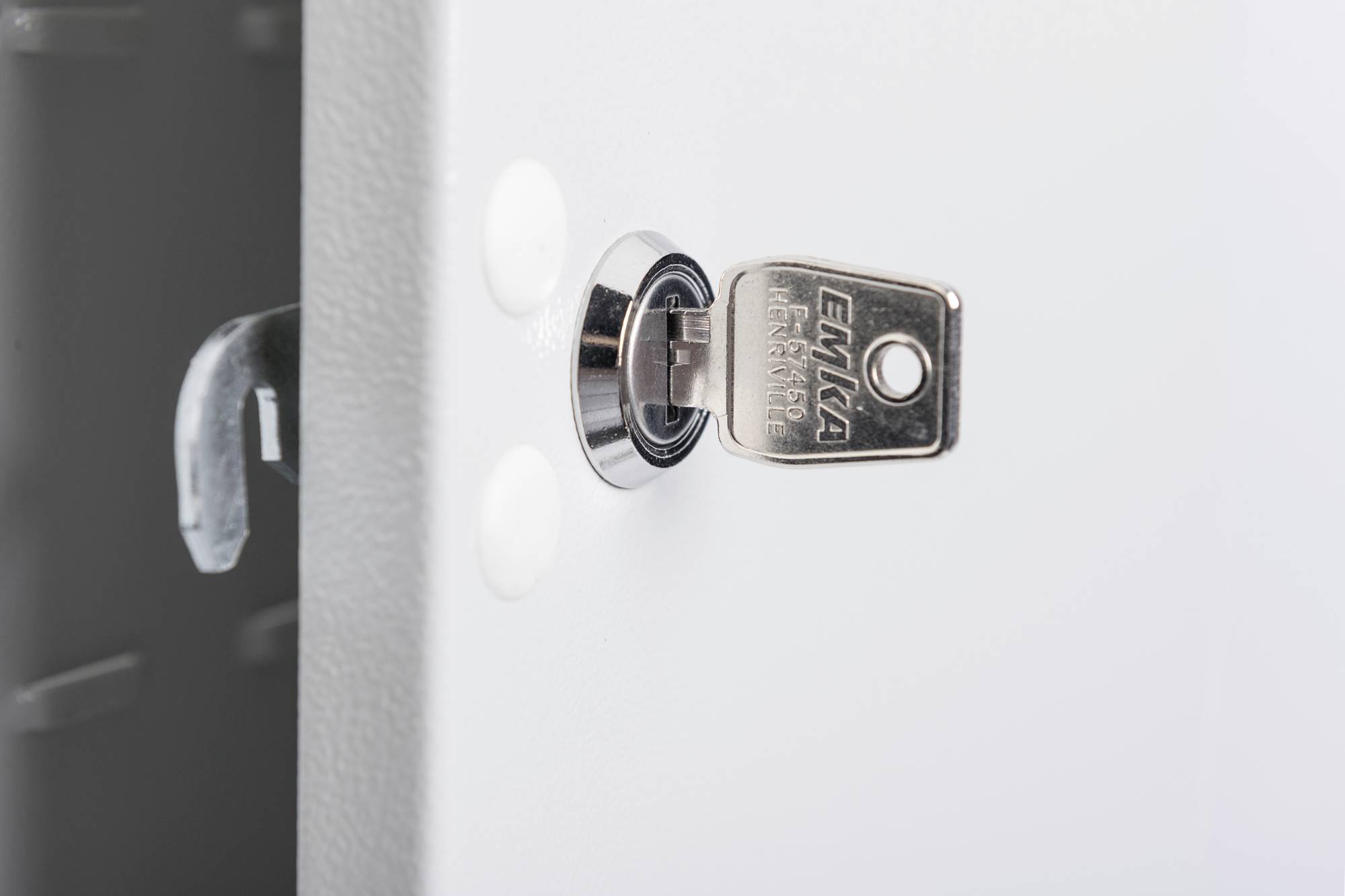 Ein Schlüssel steckt in einem Metallschloss an einer weißen Oberfläche. Das Schloss scheint Teil eines großen Objekts oder Geräts zu sein.