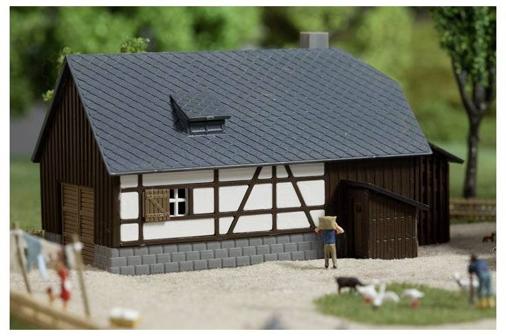 Modellbauernhof mit dunklem Dach und Fachwerkwänden, zeigt eine kleine Tür, Schornstein und Miniaturfiguren in einem gestalteten Diorama.