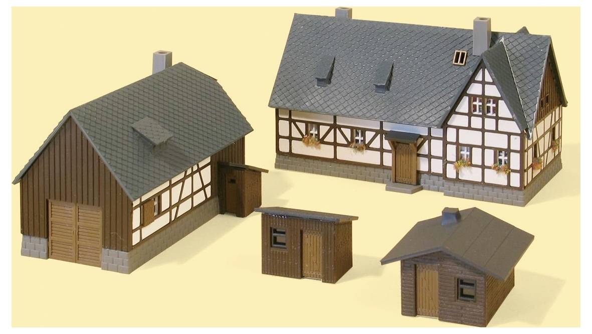 Drei Modellgebäude auf hellem Hintergrund: eine scheunenähnliche Struktur, ein Fachwerkhaus und zwei kleine Schuppen oder Nebengebäude.