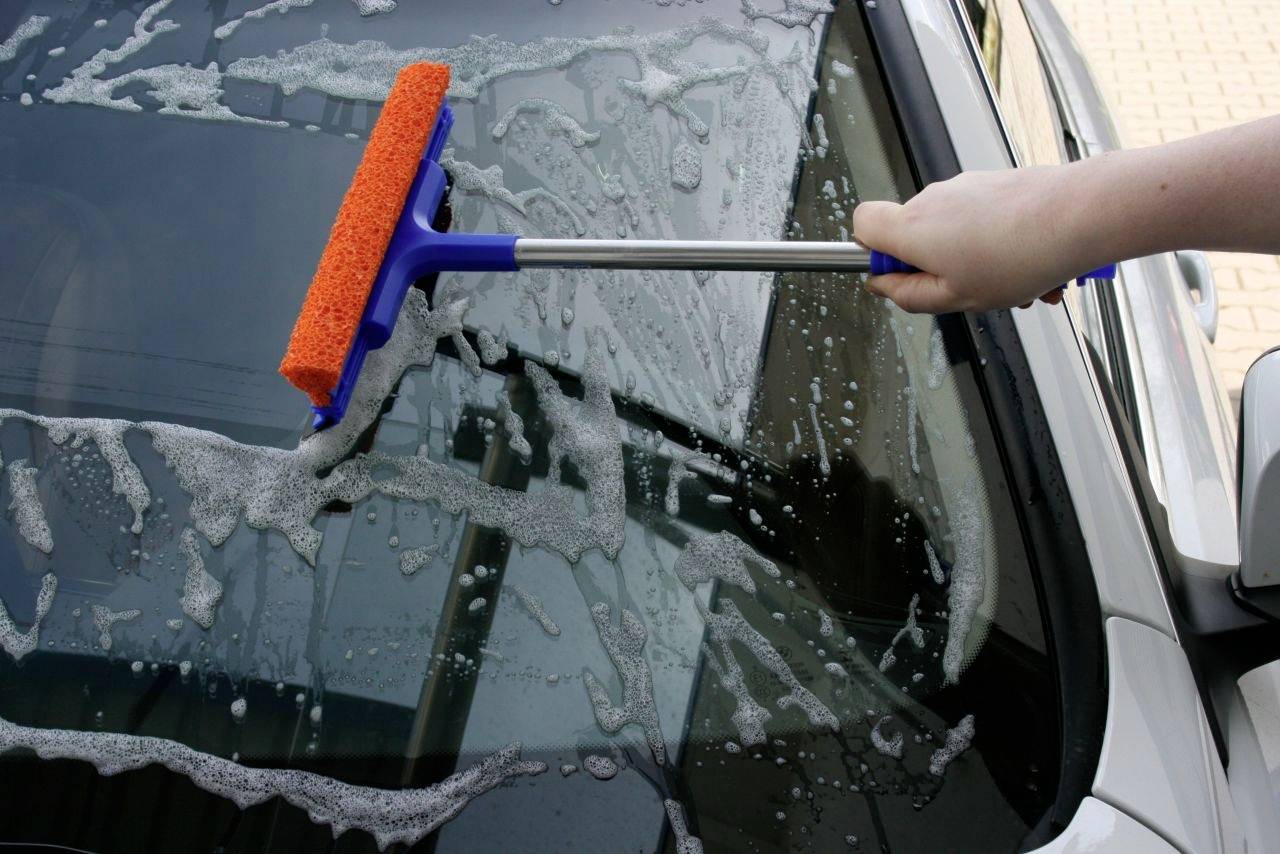 Person reinigt eine Autoscheibe mit einem Fensterwischer.