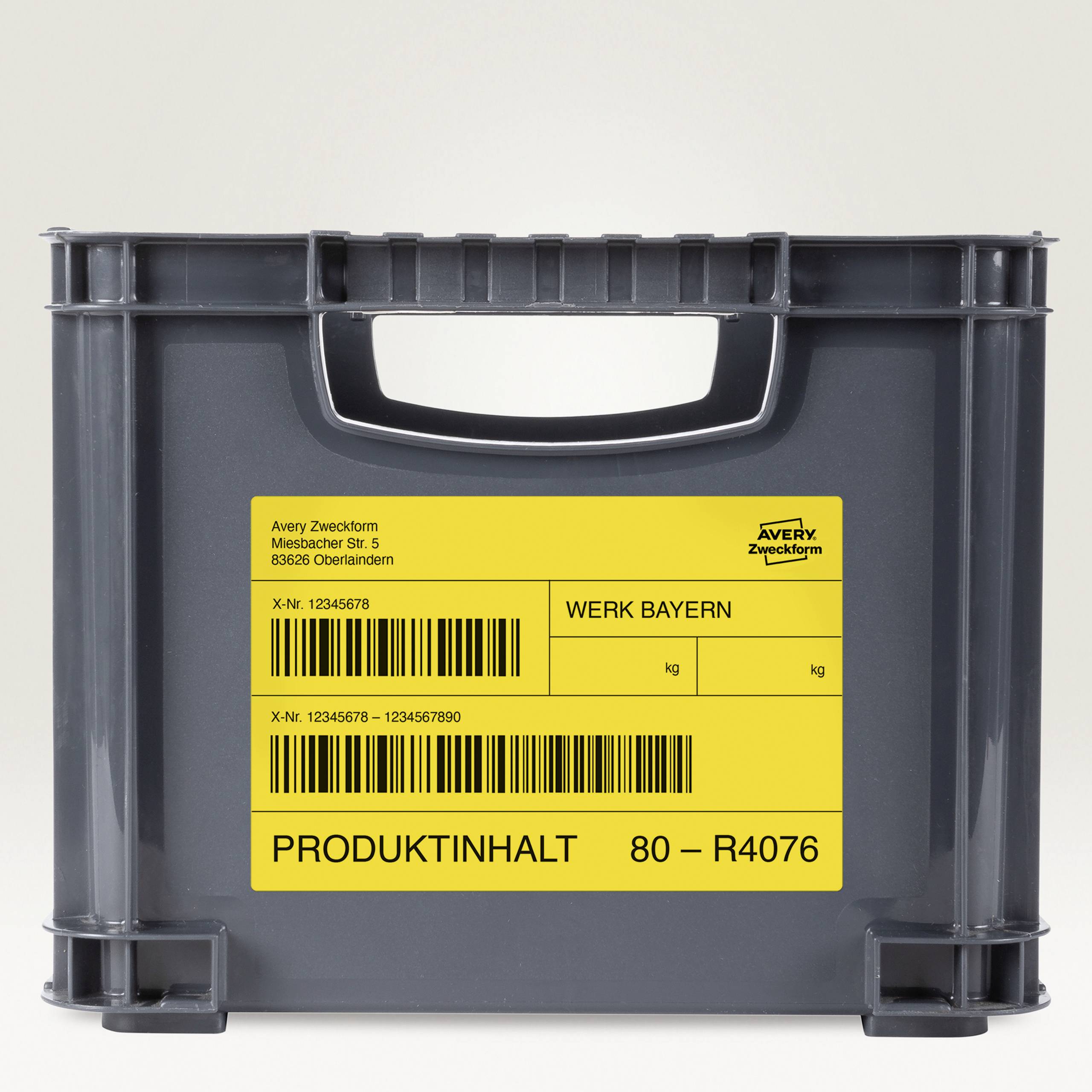 Eine graue Kunststoffkiste mit gelbem Etikett. Darauf steht: 'Werk Bayern', gefolgt von Barcodes und einer Referenznummer.