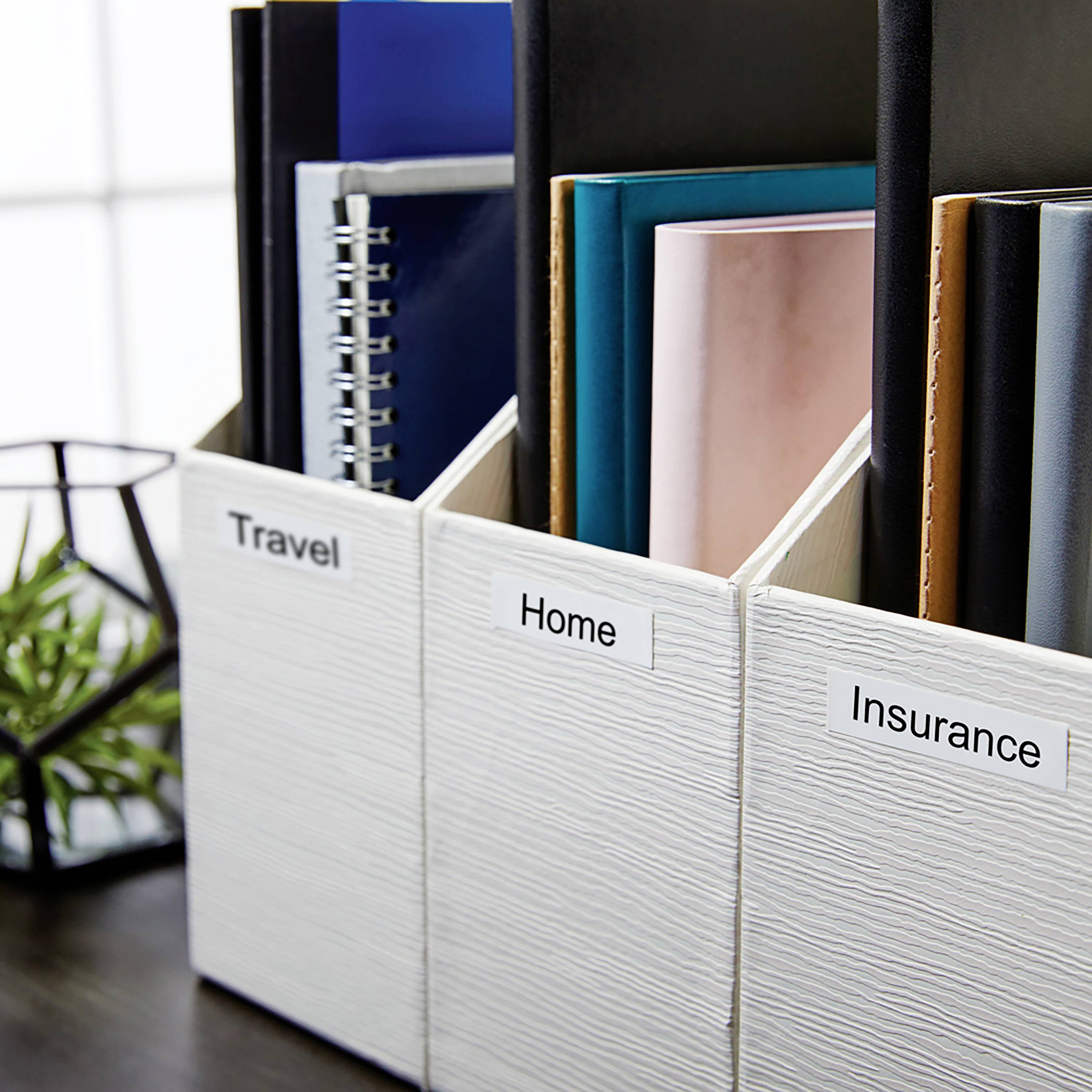 Zeigt drei beschriftete Zeitschriftenhalter: 'Travel', 'Home' und 'Insurance' mit Büchern und Ordnern darin, vor einem Fenster.