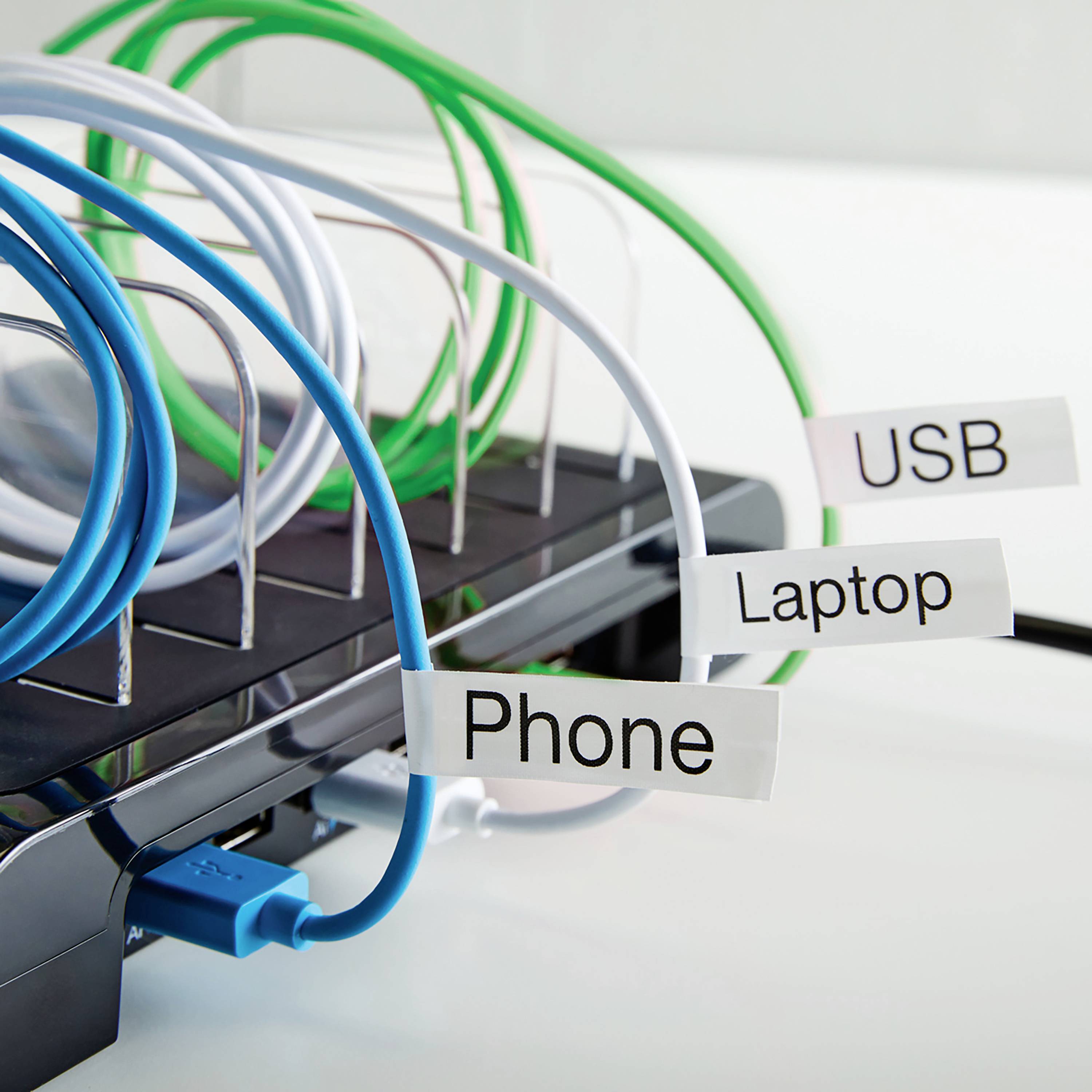 Ein Kabelhalter mit blauen, weißen und grünen Kabeln, beschriftet mit 'Phone', 'USB' und 'Laptop', organisiert mehrere Ladegeräte.