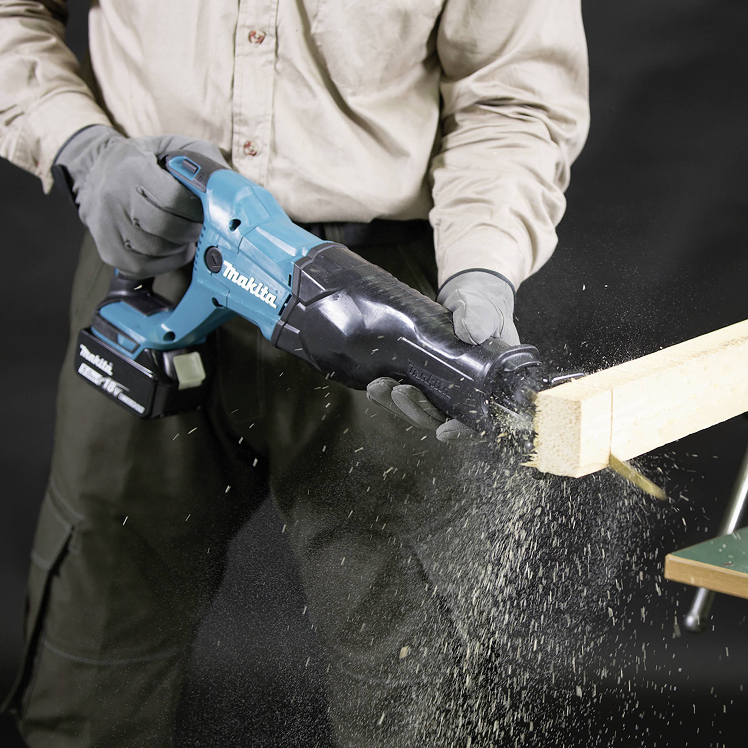 Eine Person schneidet mit einer blauen elektrischen Säbelsäge ein Holzstück. Sägespäne fliegen. Die Säge hat die Marke Makita.