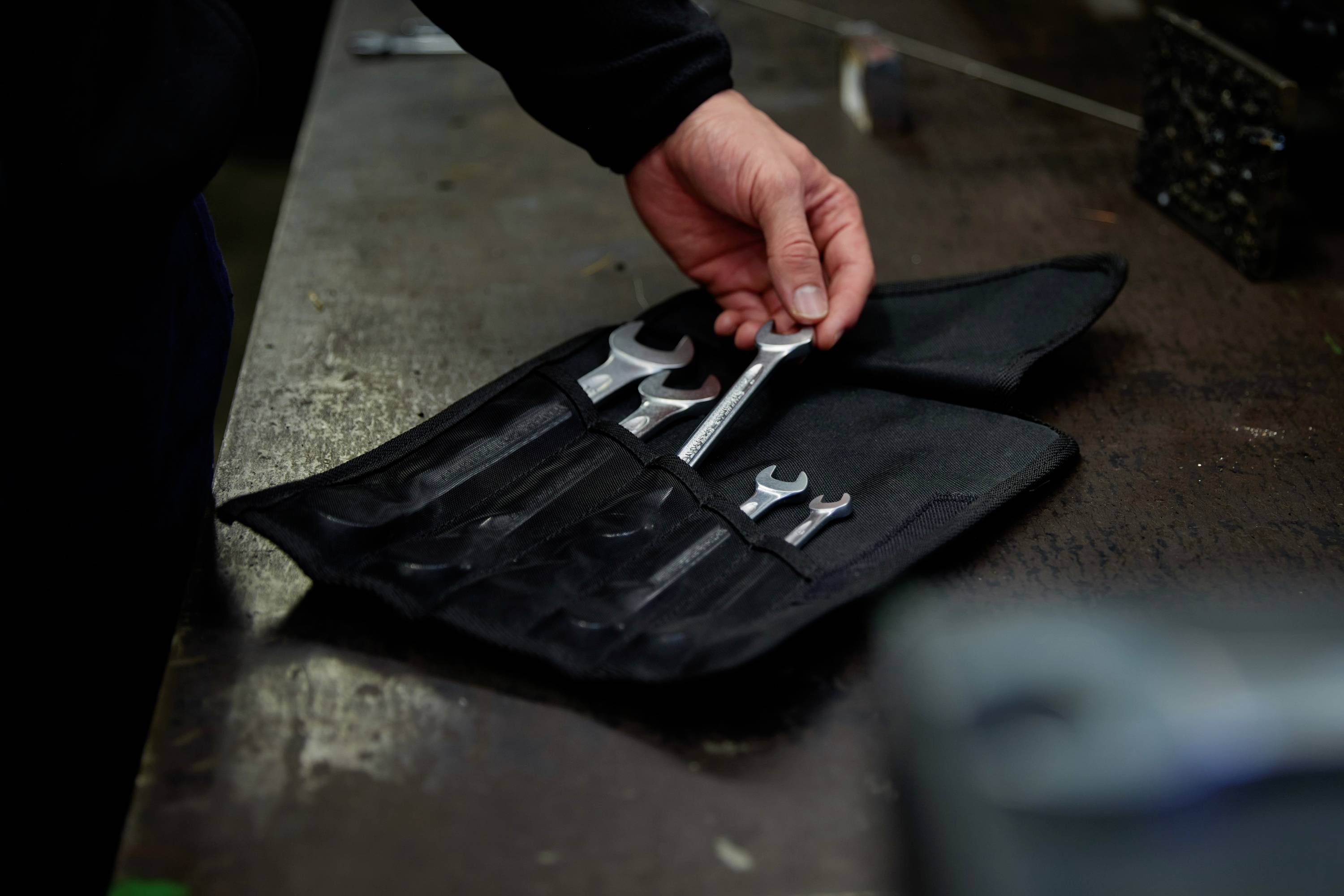 Eine Person nimmt einen Schraubenschlüssel aus einer offenen Werkzeugtasche auf einer Werkbank.