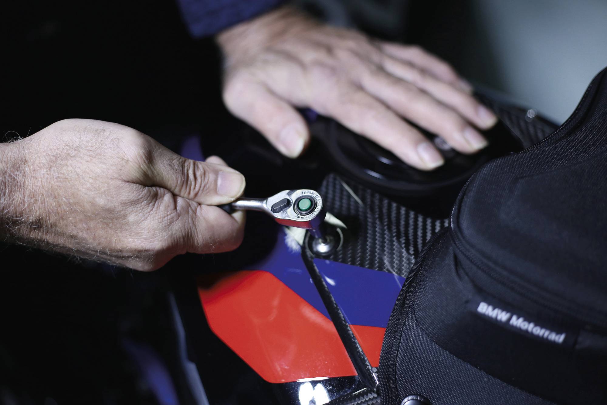 Eine Person benutzt einen Schraubenschlüssel, um ein Motorradteil einzustellen und zeigt dabei die Wartung des Fahrzeugs mit Fokus auf Werkzeuge und Hände.