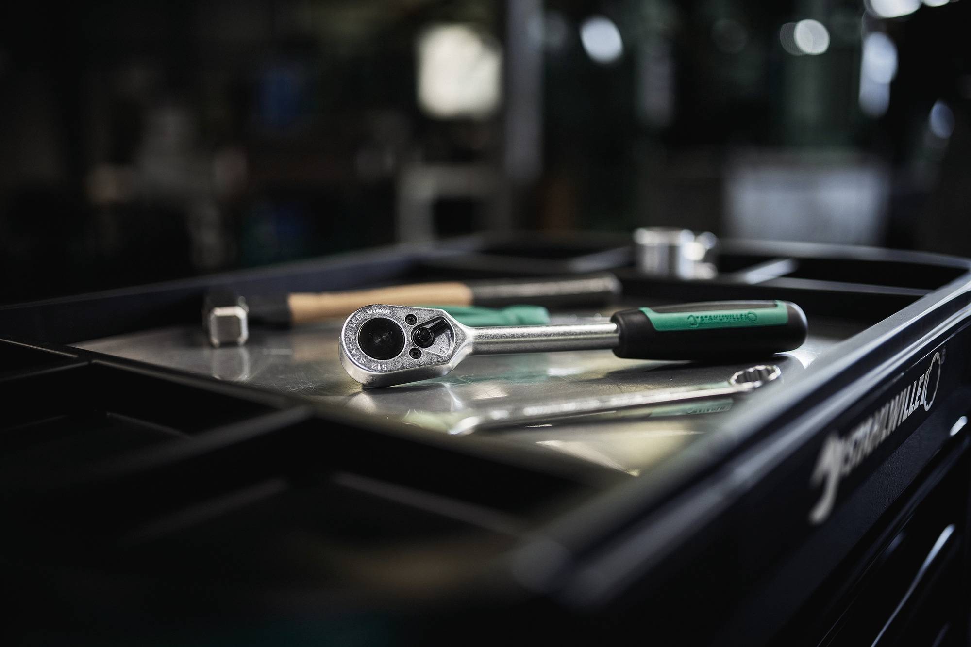 Ein Ratschenschlüssel, eine Steckdose und ein Schraubendreher auf einer Werkstatttischplatte, was eine Umgebung suggeriert, die auf mechanische Arbeit oder Reparatur ausgerichtet ist.