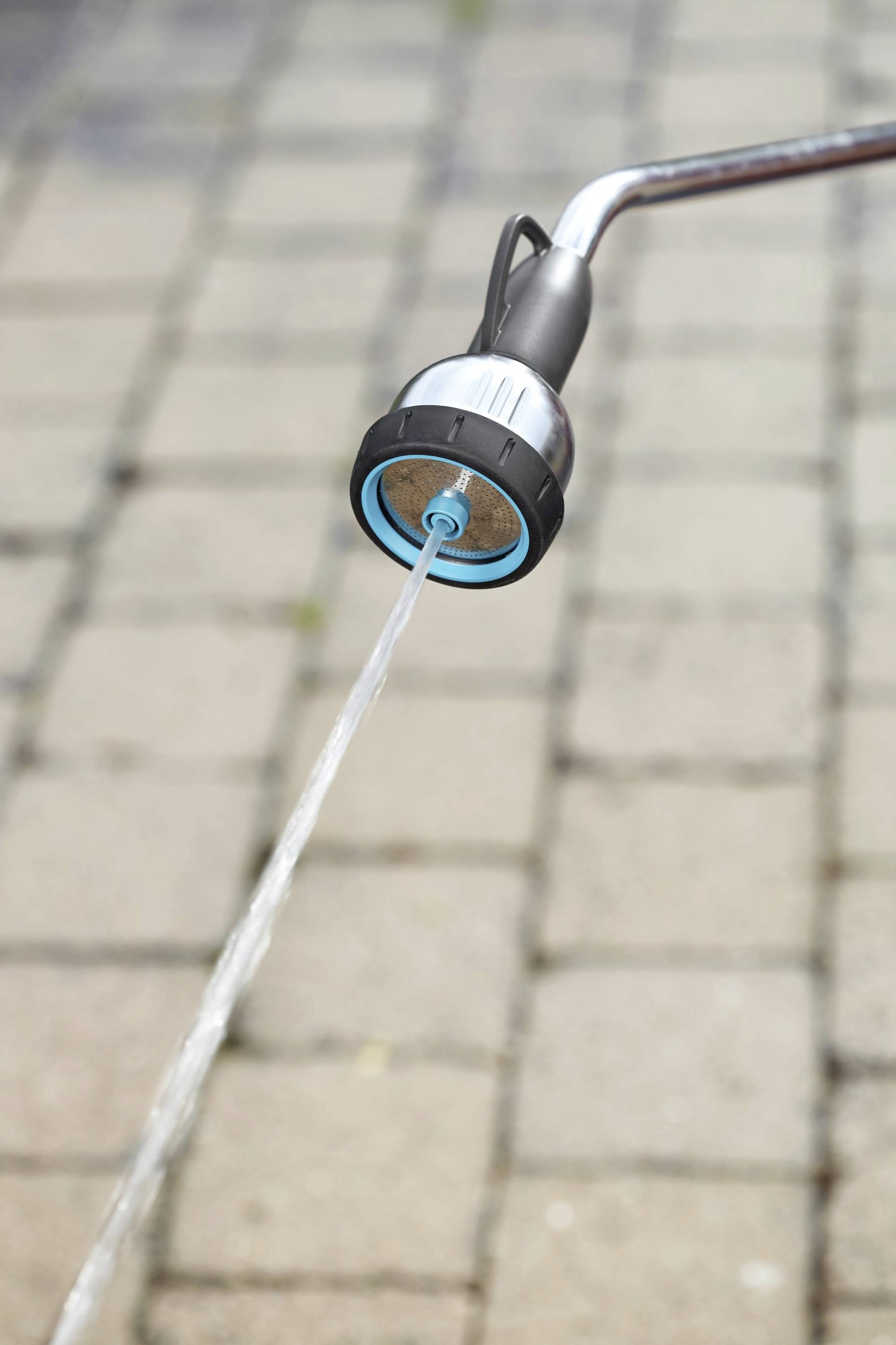 Ein Wasserschlauch sprüht einen Wasserstrahl auf eine gepflasterte Fläche.