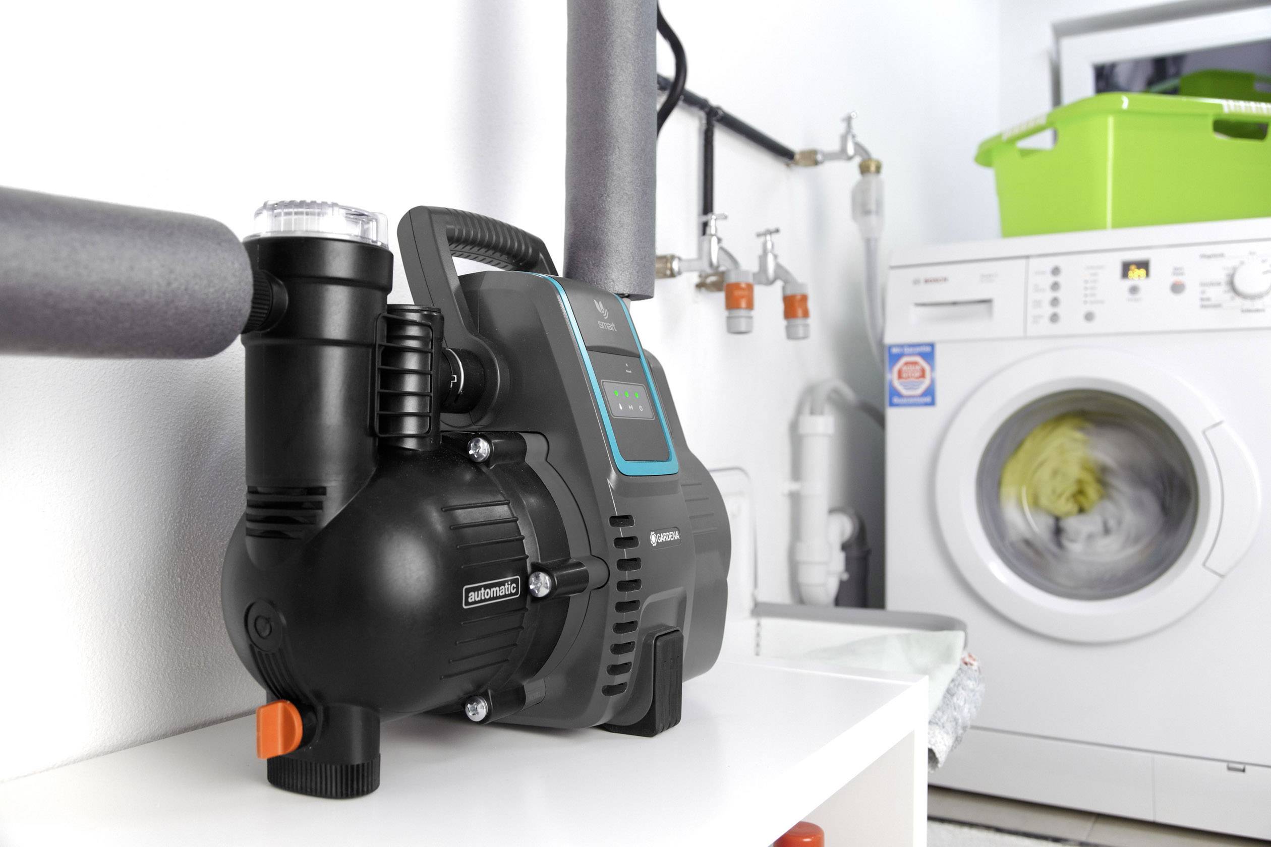 Schwarze, elektrische Wasserpumpe auf weißem Regal neben einer laufenden Waschmaschine in einem Hauswirtschaftsraum.