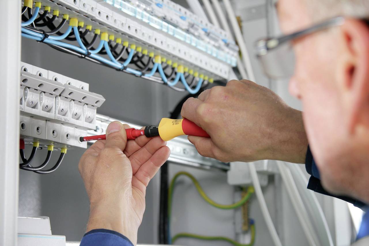 Ein Elektriker arbeitet mit einem Schraubendreher an einem Sicherungskasten, um elektrische Verbindungen zu installieren oder warten.