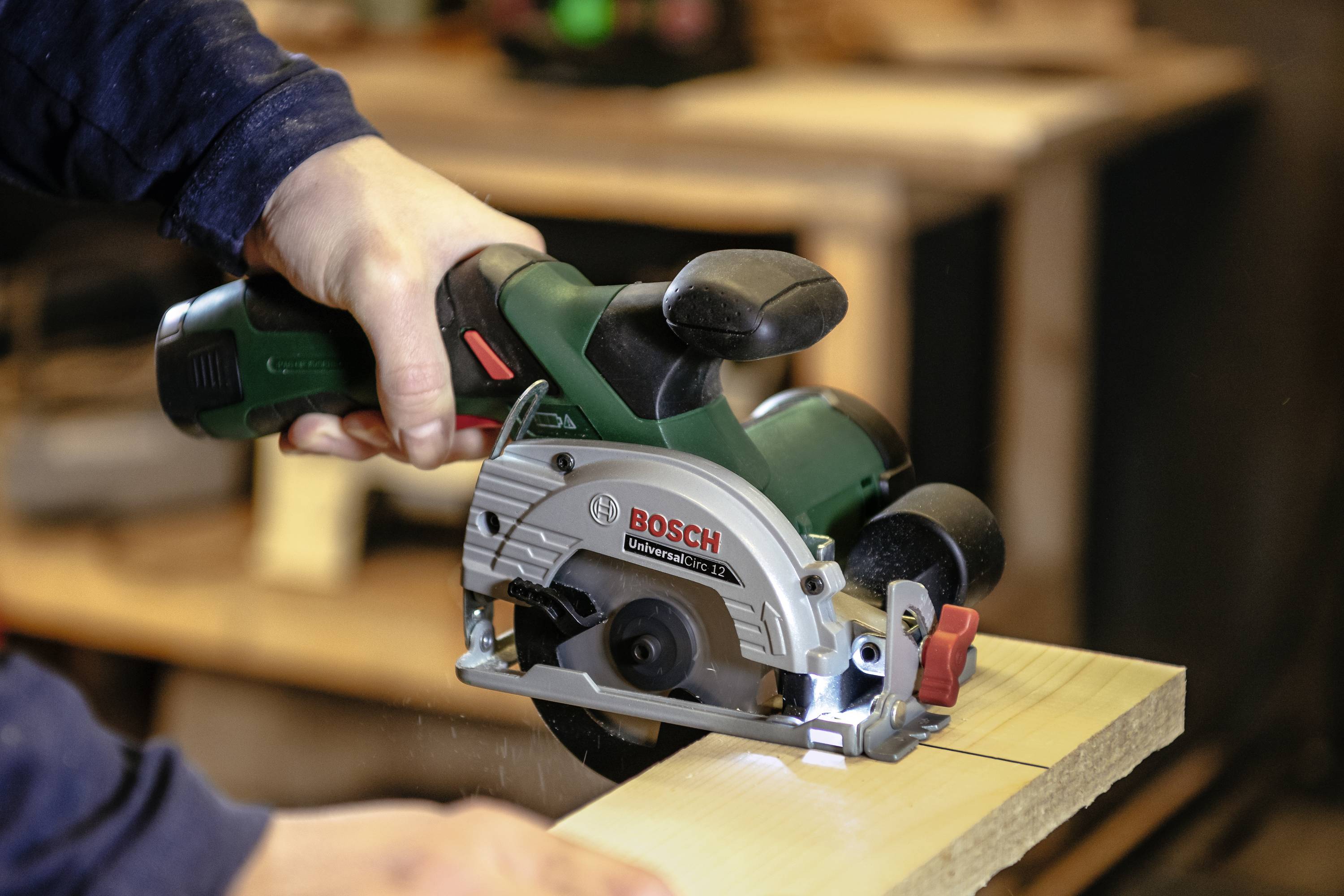 Eine Person sägt ein Holzbrett mit einer Bosch-Handkreissäge in einer Werkstattumgebung.