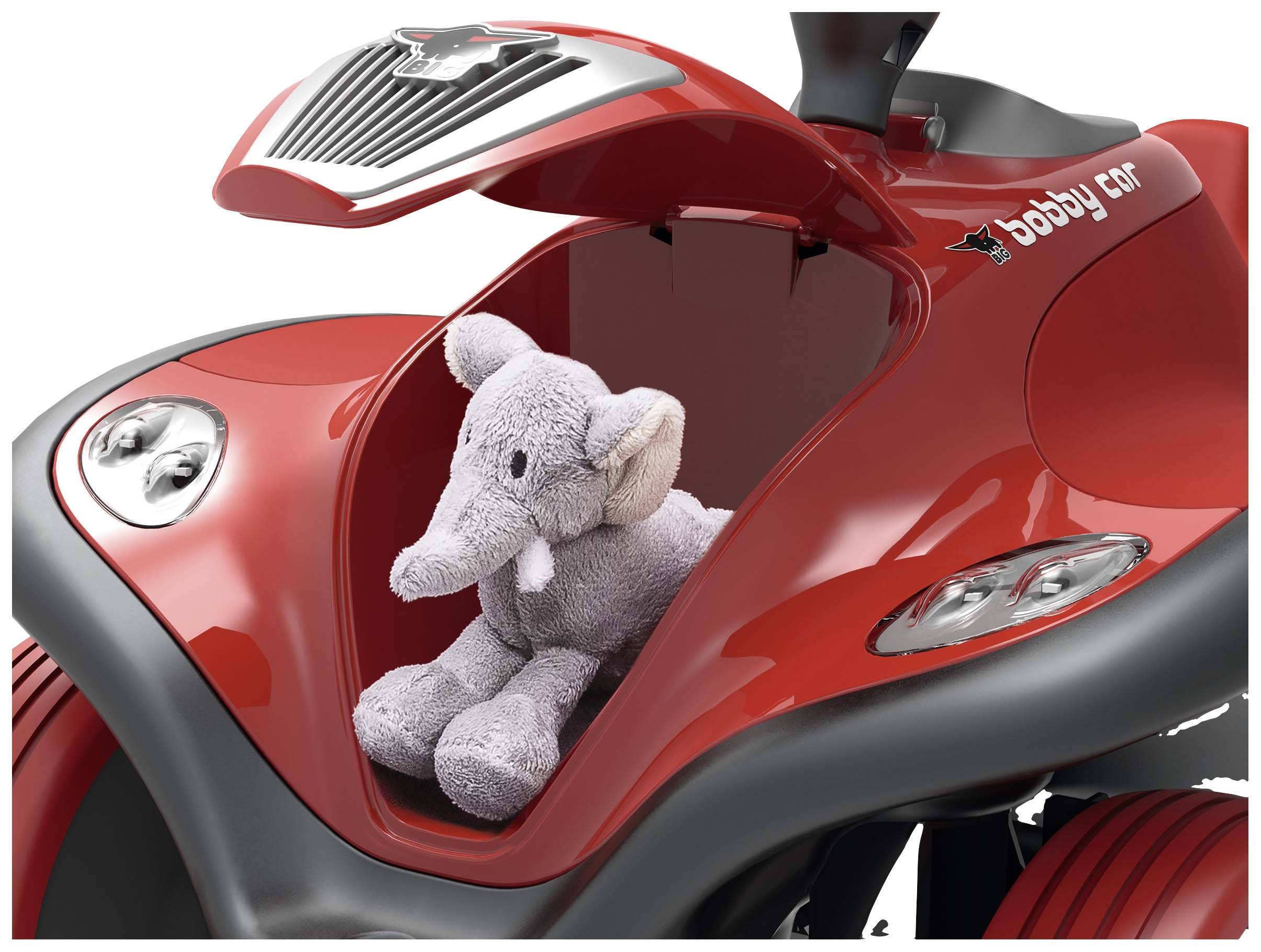 Rotes Spielzeugauto mit offenem Kofferraum. Ein grauer Plüschelefant sitzt darin.