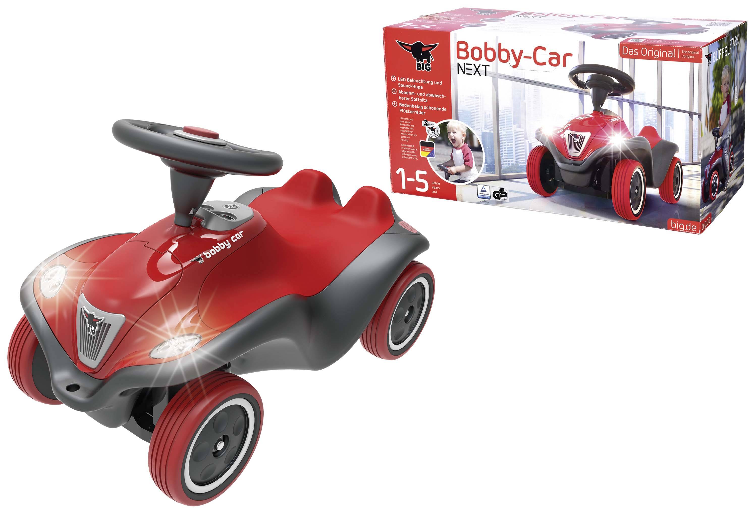 Rotes Kinderfahrzeug 'Bobby-Car NEXT' mit schwarzen Akzenten und LED-Lichtern, geeignet für Kinder von 1 bis 5 Jahren. Verpackung im Hintergrund.