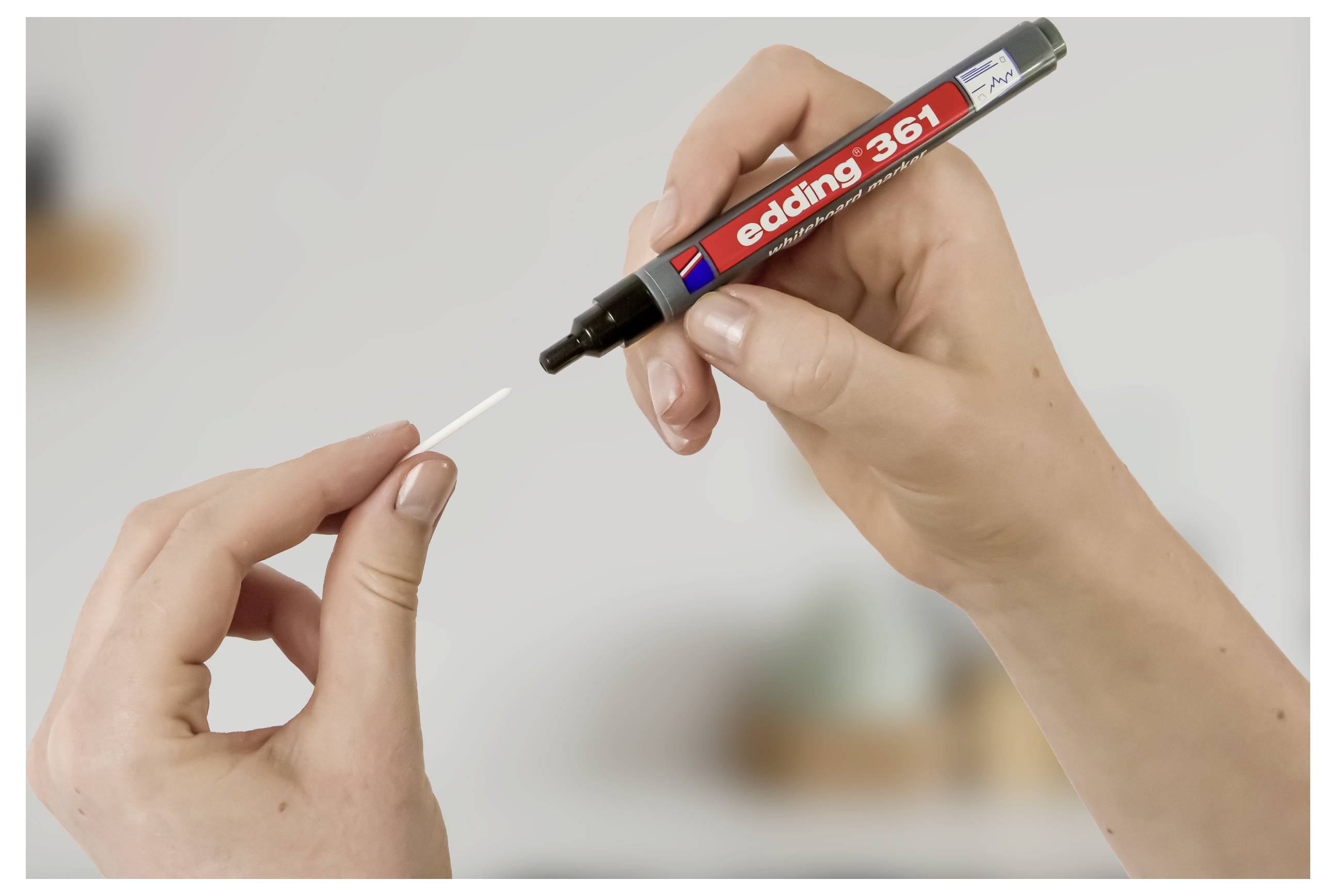 Hände halten einen „edding 361"-Marker und einen weißen Wattestäbchen, wobei die Spitze gegen das Wattestäbchen angewendet wird, mit unscharfem Hintergrund.