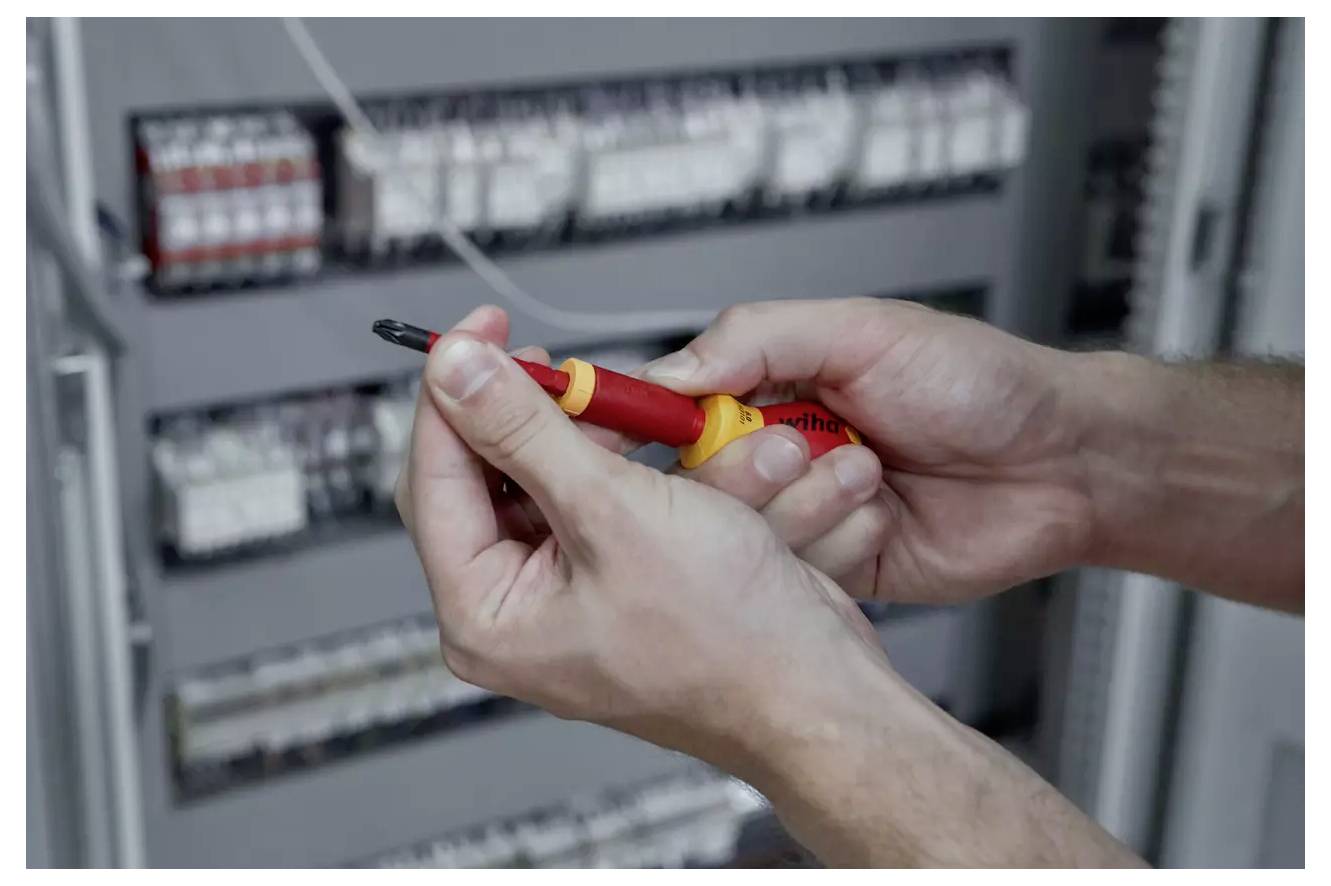 Eine Person verwendet einen isolierten Schraubenzieher, um an einem Schaltschrank zu arbeiten, wobei der Fokus auf Sicherheit und Präzision liegt.