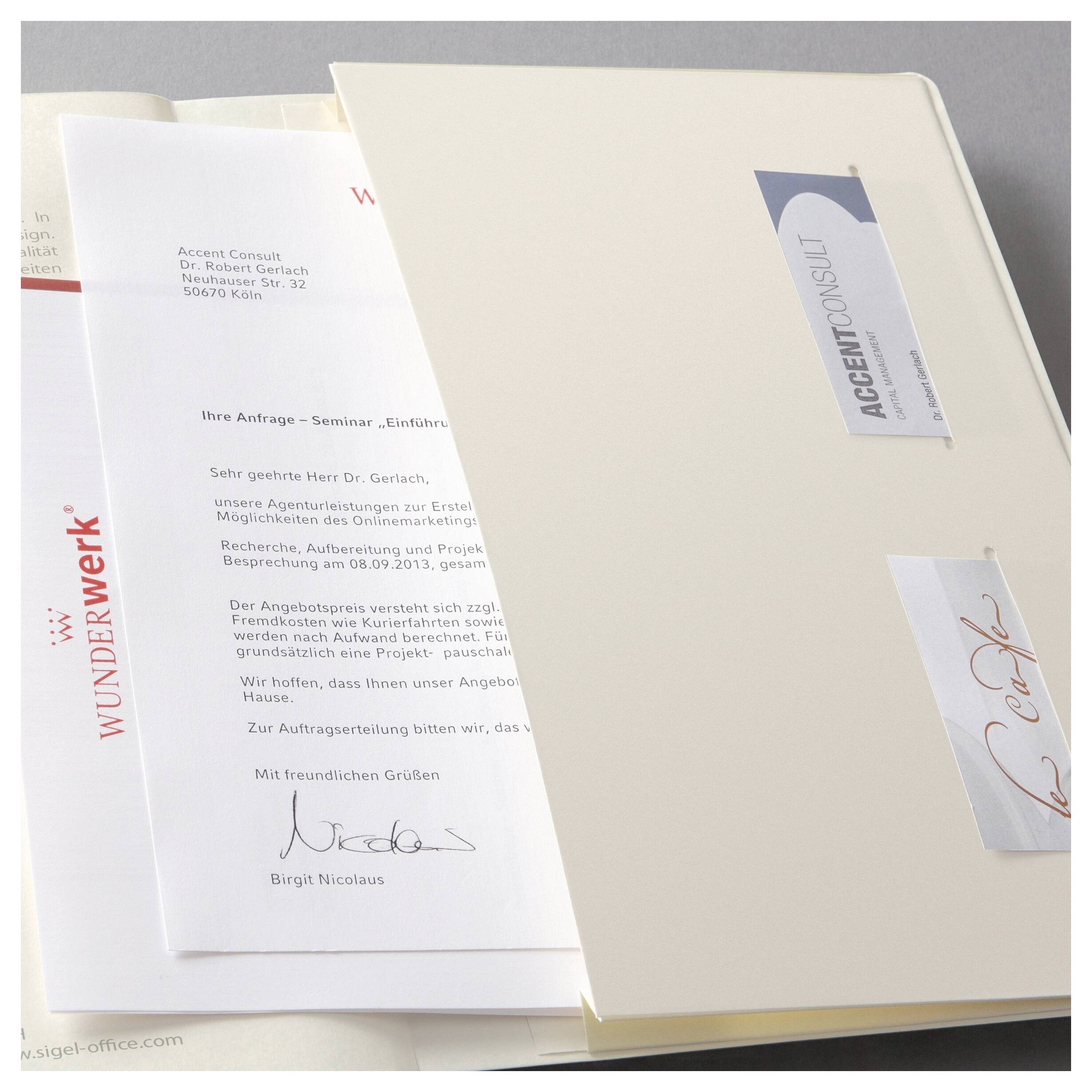 Ein offener Ordner mit einem deutschen Geschäftsbrief und zwei beschrifteten Beilagen, was auf ein formelles Angebot oder Dokumentpaket hindeutet.