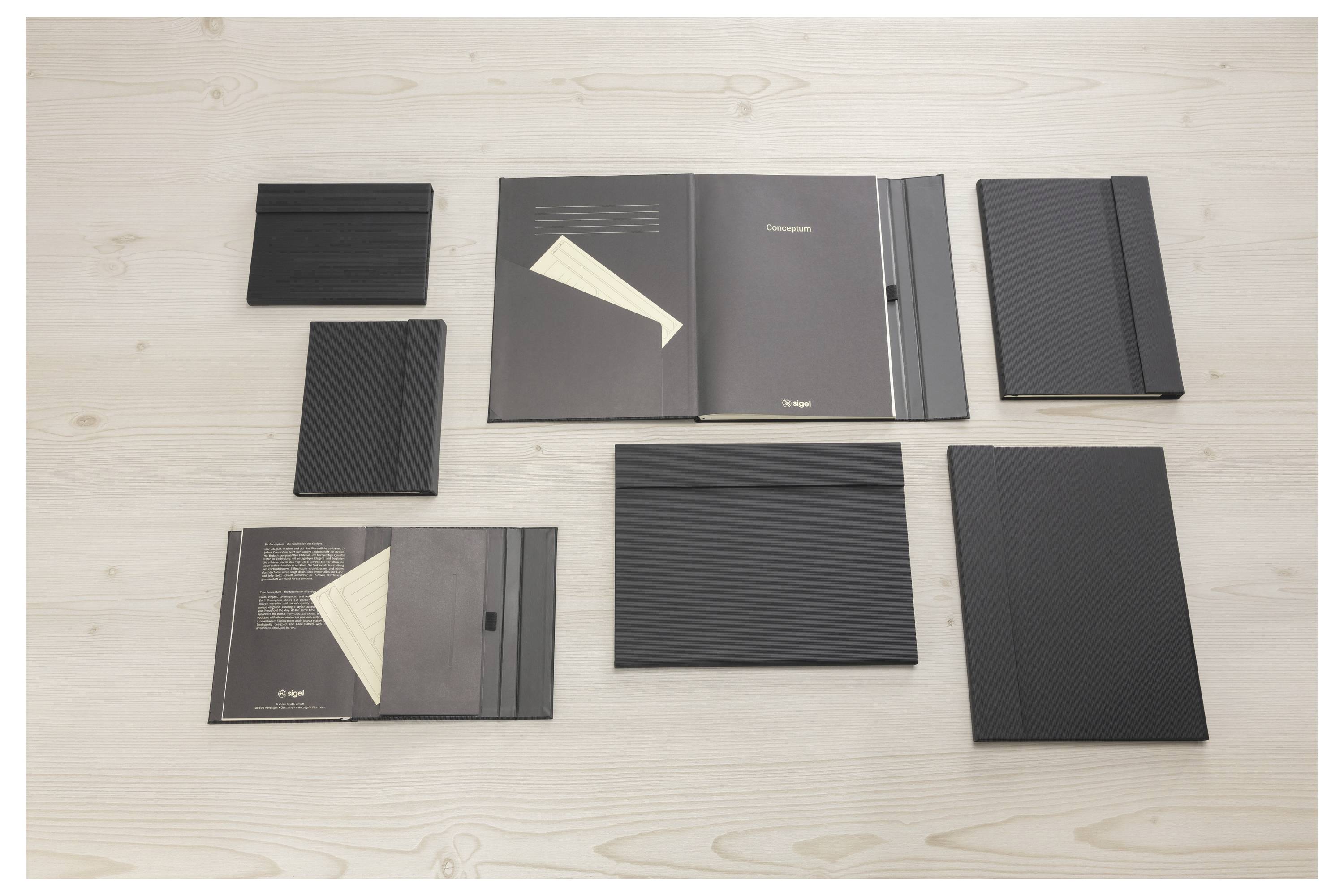 Sechs schwarze Präsentationsmappen und Broschüren auf einer hellen Holzoberfläche angeordnet, die verschiedene Größen und Coverdesigns zeigen.