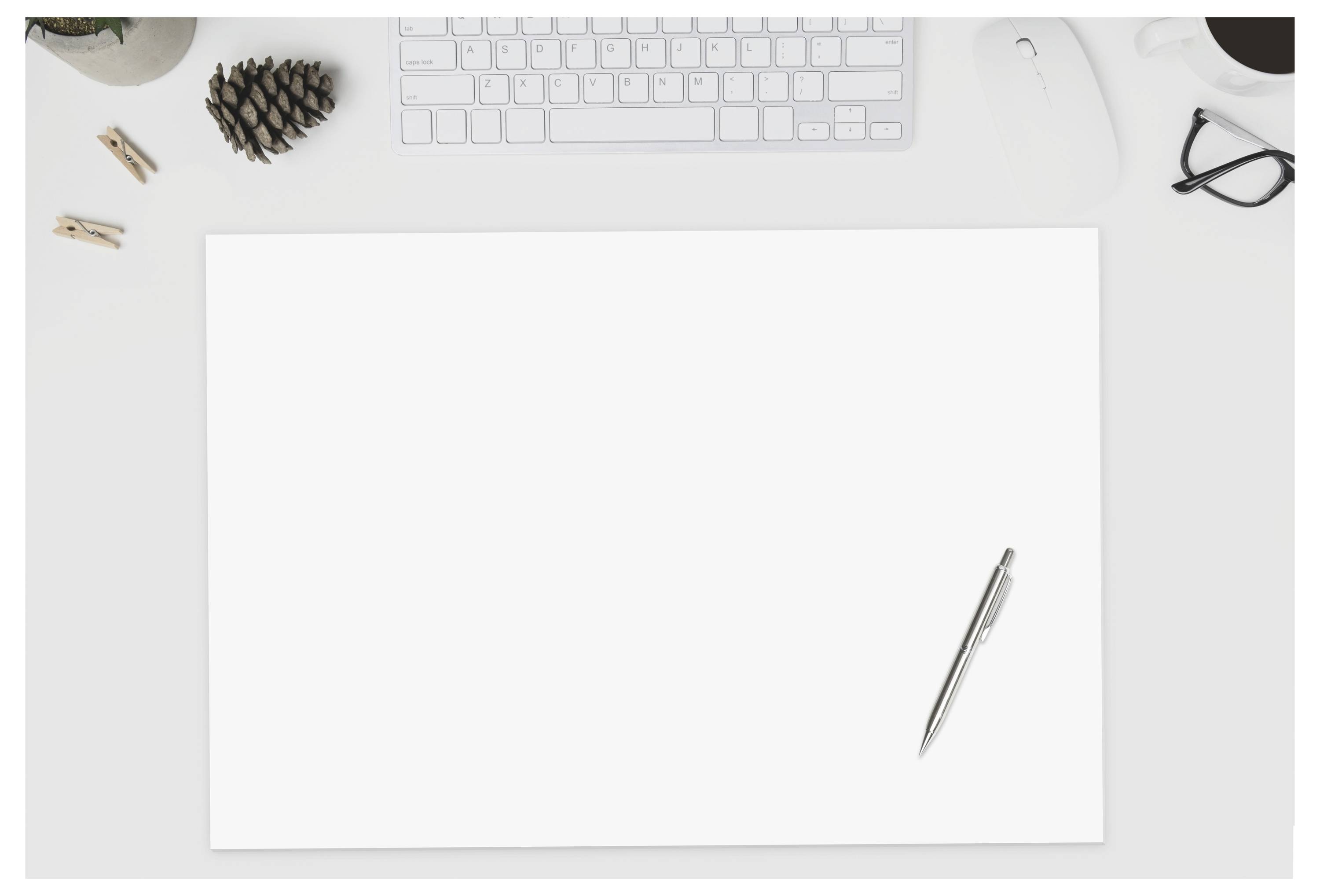 Leeres weißes Blatt Papier auf einem Schreibtisch mit einem Stift, einer Tastatur, einer Brille und kleinen Büroartikeln herum.