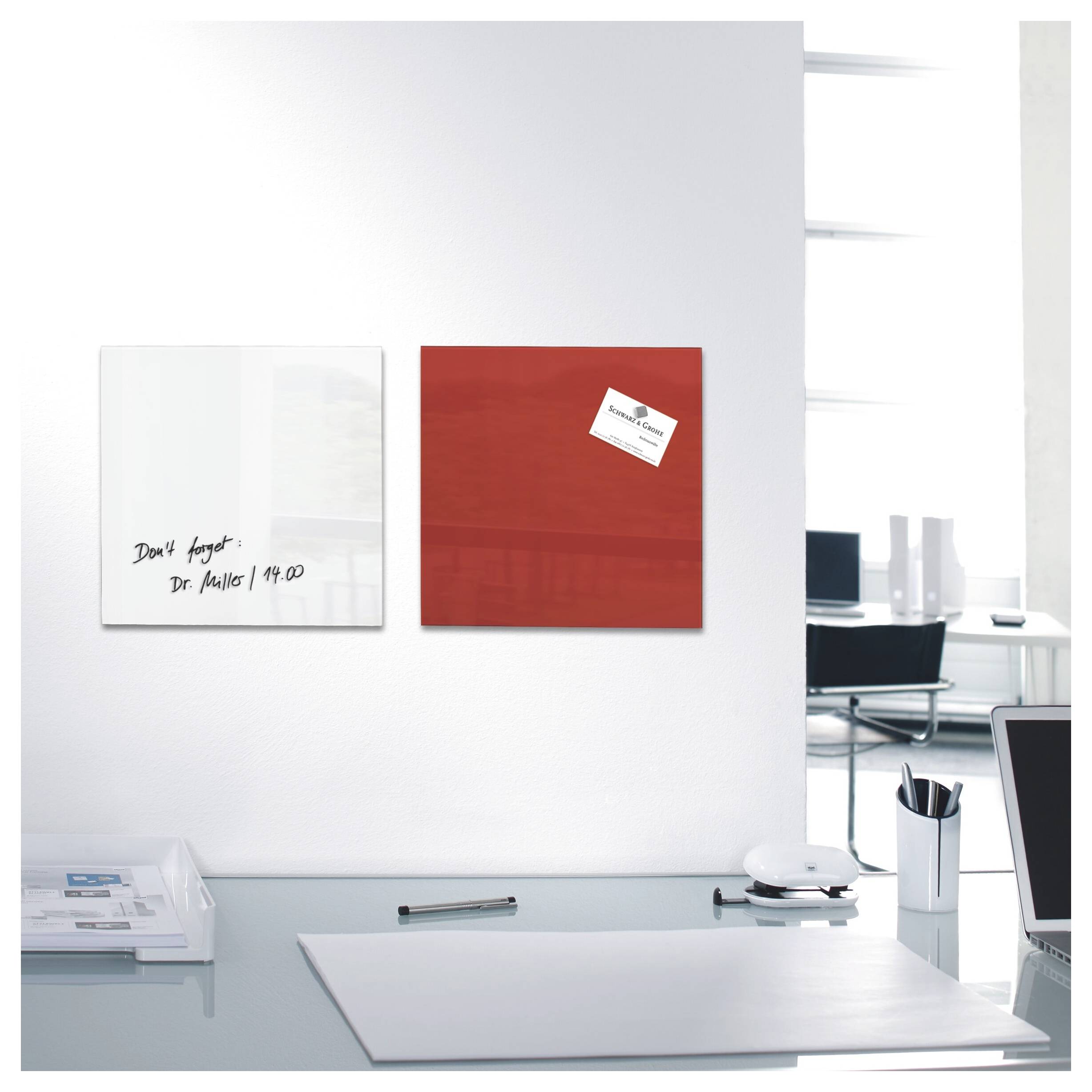 Moderner Schreibtisch mit zwei an der Wand befestigten quadratischen Tafeln, eine weiße mit handschriftlicher Notiz und eine rote mit einer kleinen Visitenkarte