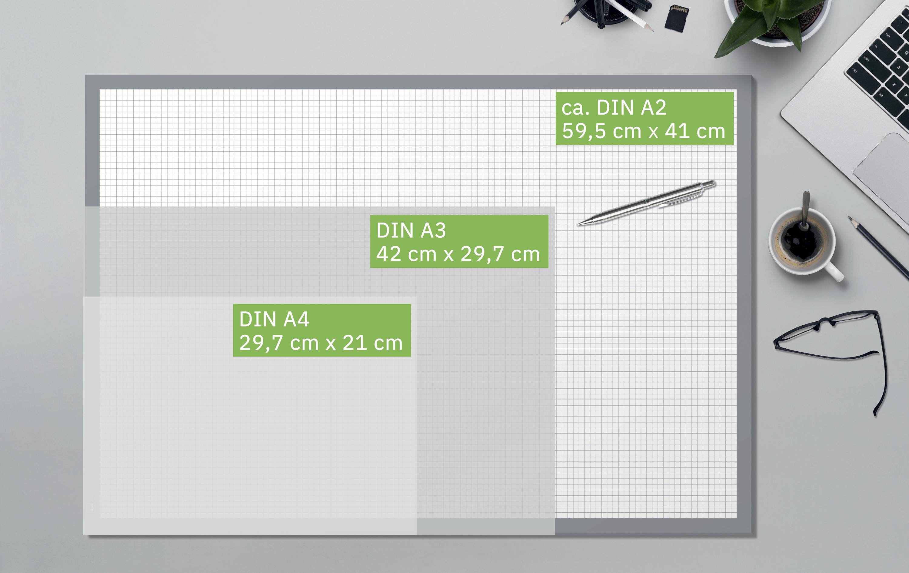 Vergleich von Papiergrößen: DIN A2, 59,5 x 41 cm; DIN A3, 42 x 29,7 cm; DIN A4, 29,7 x 21 cm. Laptop, Brille und Pflanze ergänzen das Bild.