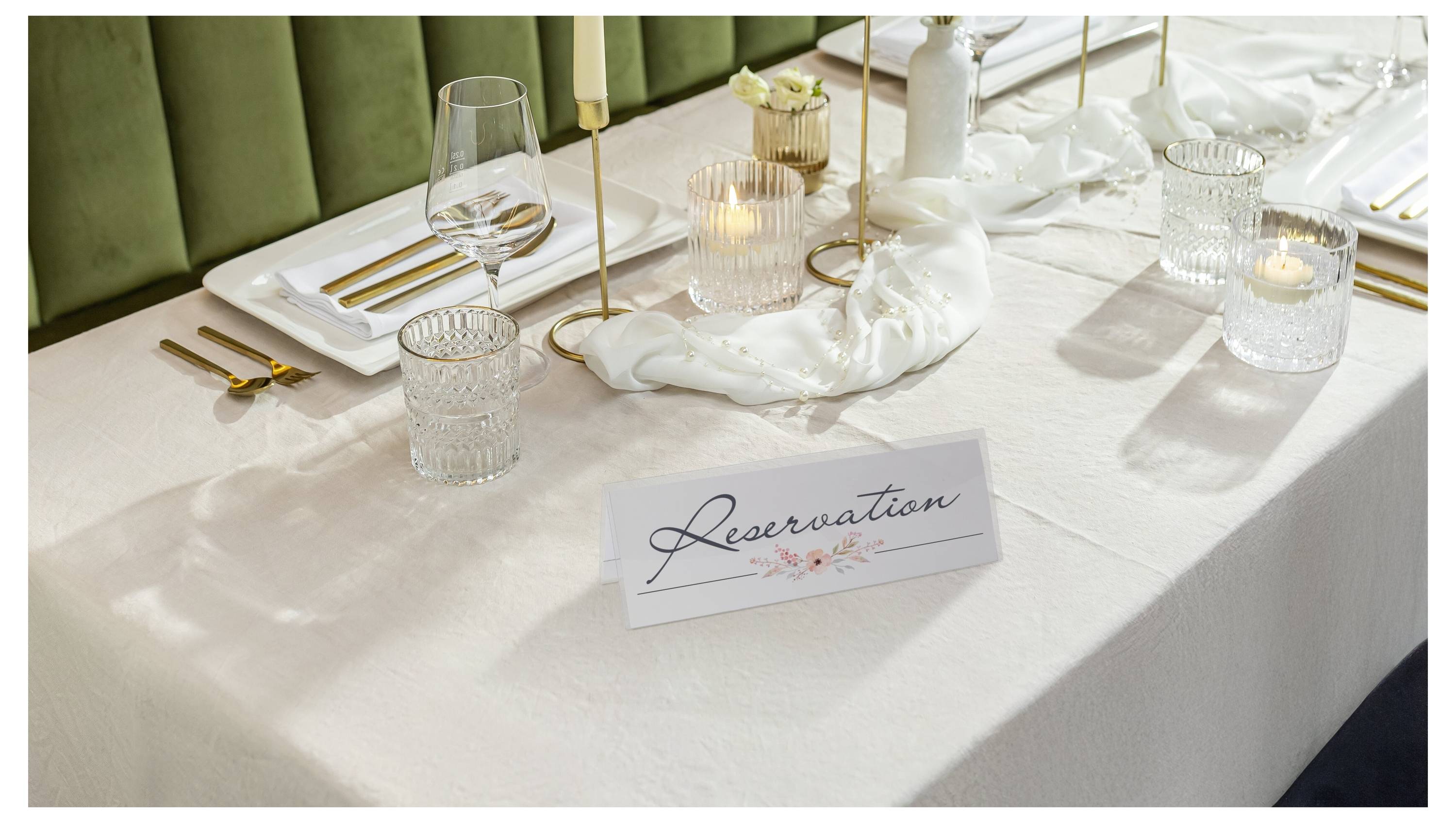 Eleganter Esstisch für ein reserviertes Event eingedeckt, mit einer Reservierungskarte, Kerzen, Glaswaren, Servietten und goldbesteck.