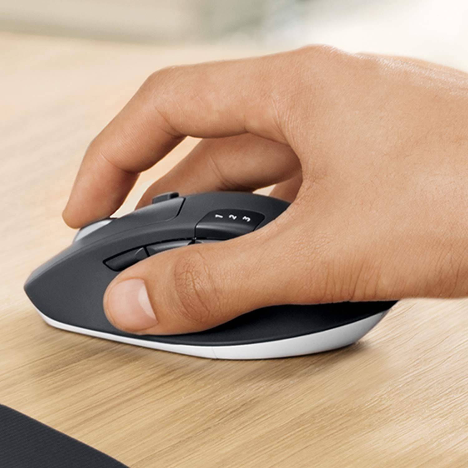 Eine Hand bedient eine kabellose Computermaus auf einem Holztisch. Die Finger ruhen auf den Tasten der Maus.
