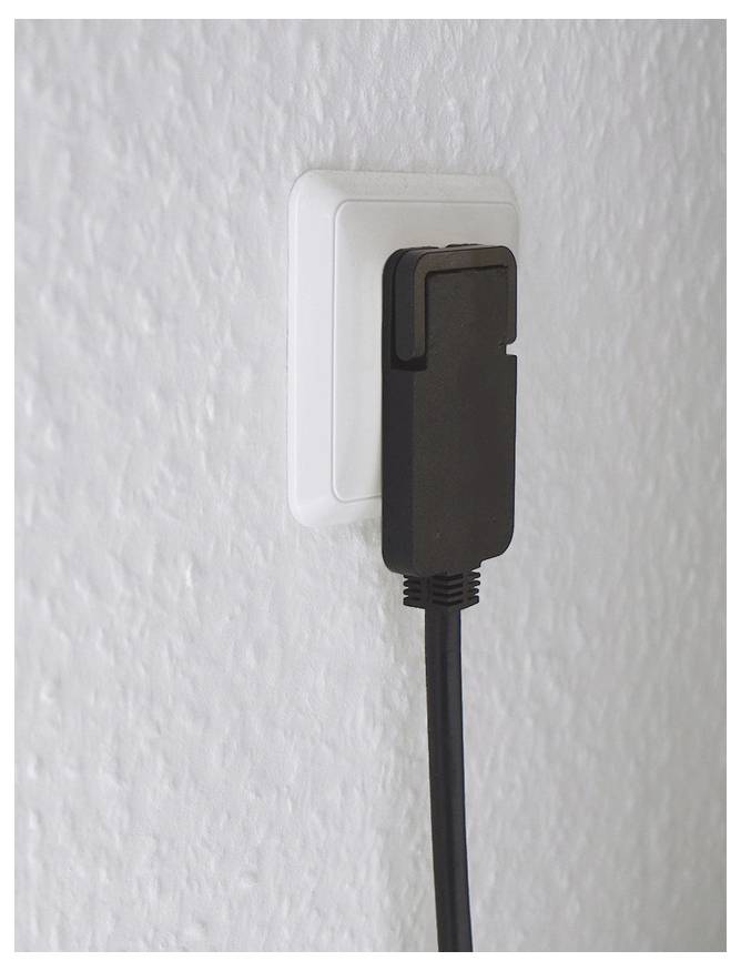 Schwarzer Stromadapter in einer weißen Steckdose an einer strukturierten Wand angeschlossen