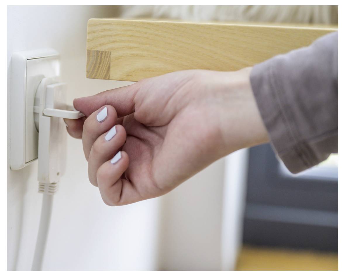 Nahaufnahme einer Hand, die ein weißes Kabel in eine Steckdose neben einem Holztisch einsteckt.