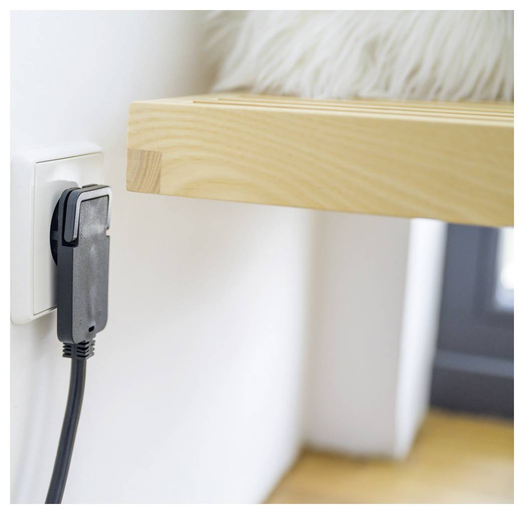 Nahaufnahme eines schwarzen Steckers, der in eine Wandsteckdose neben einer Holztischplatte eingesteckt ist, zeigt ein angeschlossenes Stromkabel in einem Raum.