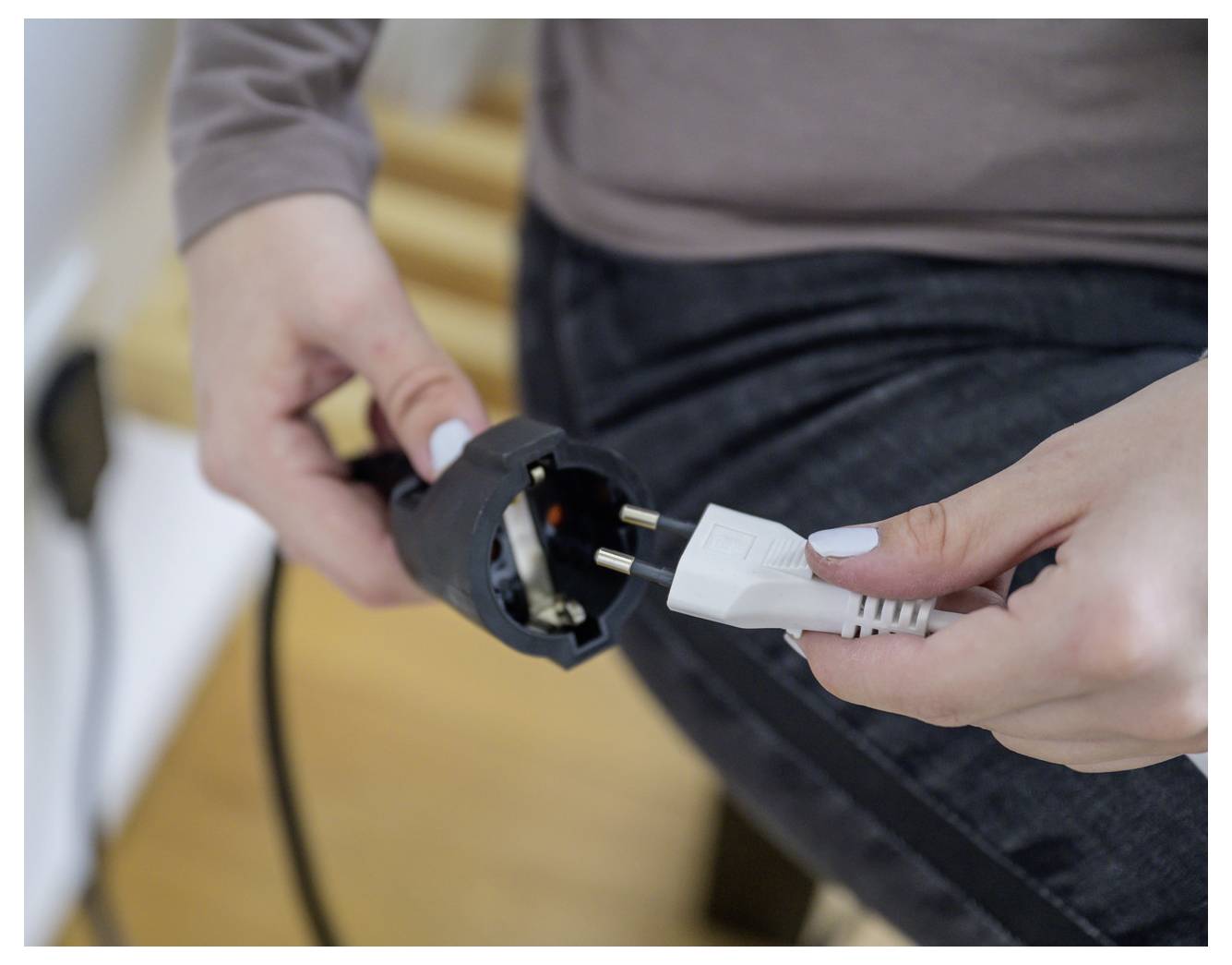 Eine Person steckt ein weißes Stromkabel in einen schwarzen Stromanschluss oder Stecker, den sie mit beiden Händen hält.