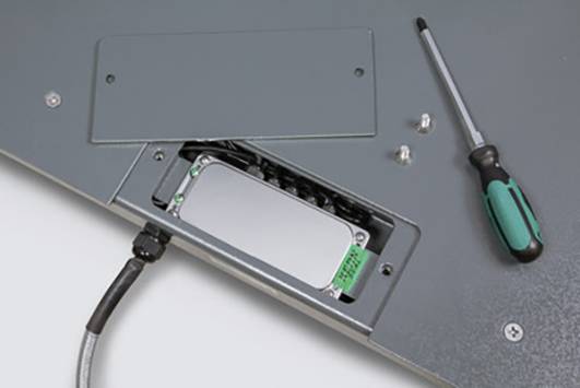 Ein Schraubendreher liegt neben einer geöffneten Metallklappe, die eine angeschlossene elektronische Komponente freilegt.