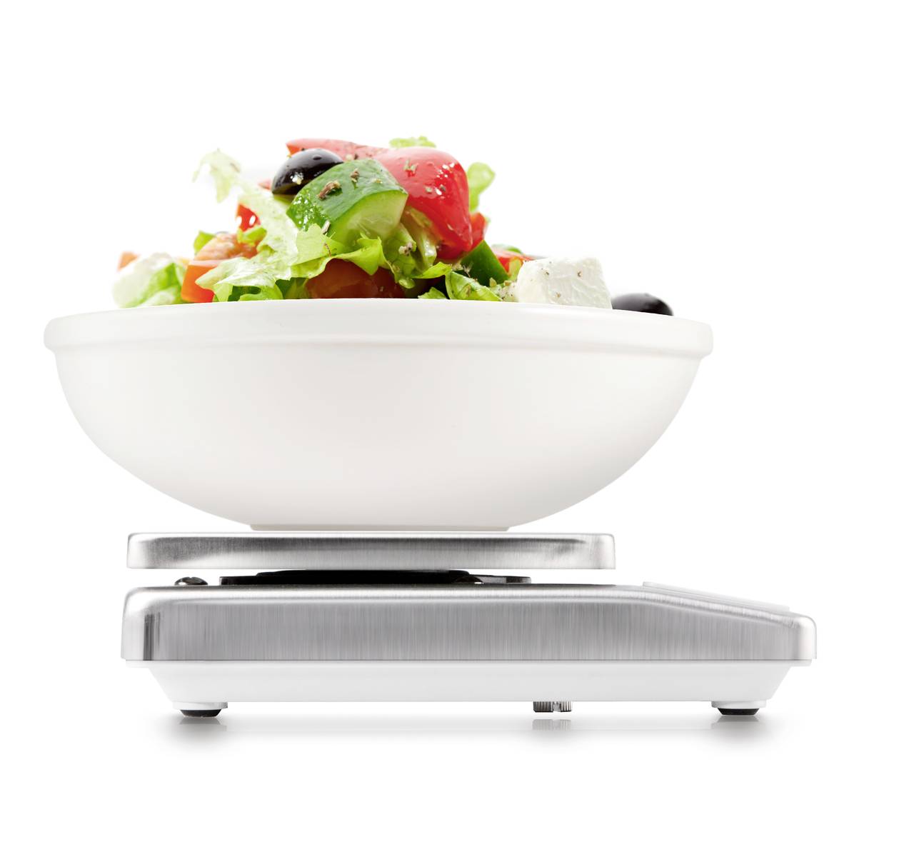 Eine weiße Schüssel mit Salat, bestehend aus Tomaten, Oliven, Feta und Blättern, steht auf einer digitalen Küchenwaage.