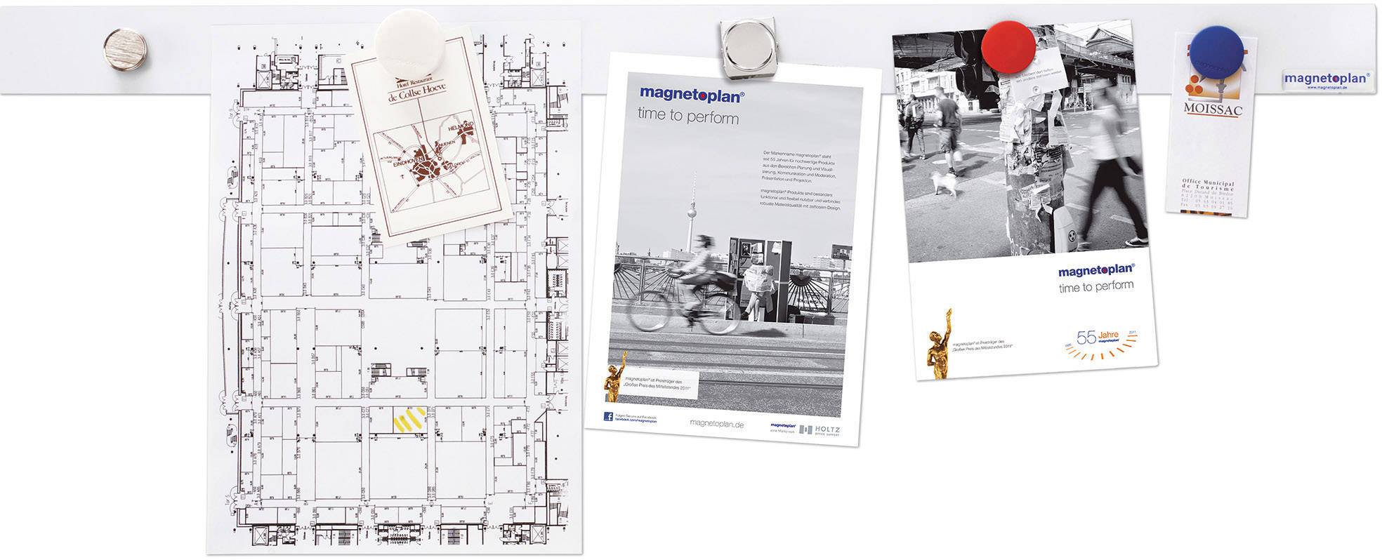 Ein Architekturplan an einer Pinnwand, daneben drei Fotos und ein Kalenderblatt befestigt mit bunten Magneten.