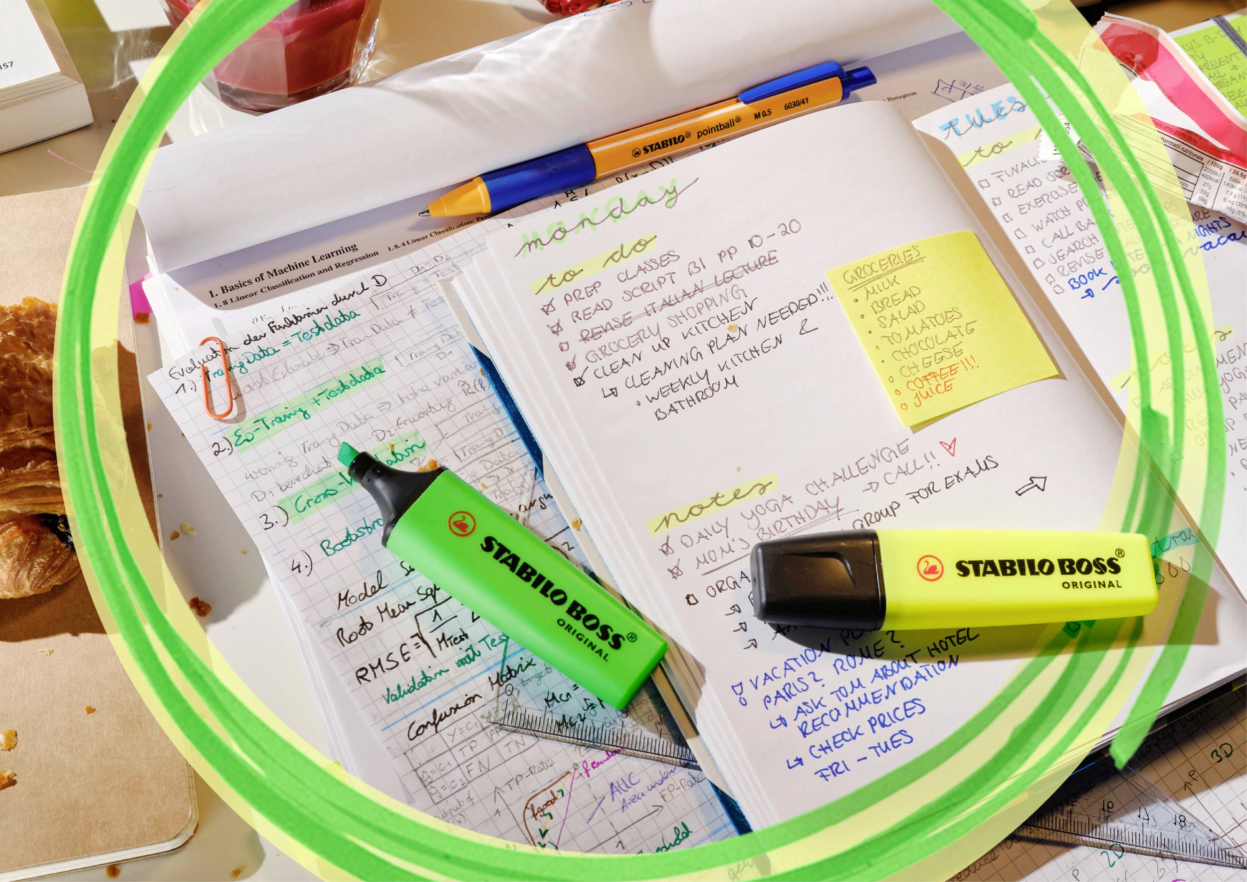 Notizbuch mit handgeschriebenen Notizen in verschiedenen Farben. Verschiedene Textmarker und ein Stift sind auf dem Tisch verteilt.