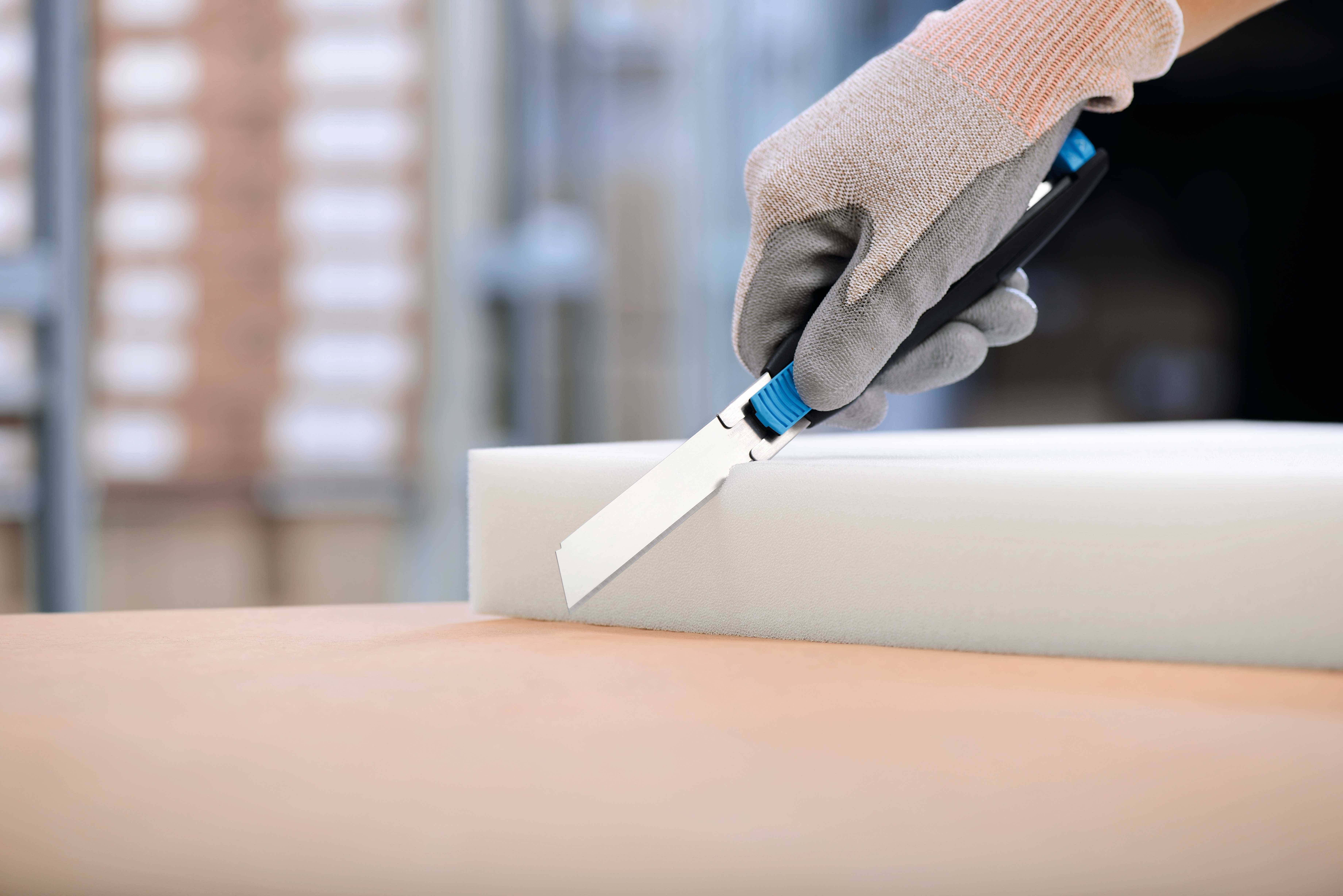 Eine Person mit Handschuhen schneidet mit einem Messer präzise einen weißen Schaumstoffblock.