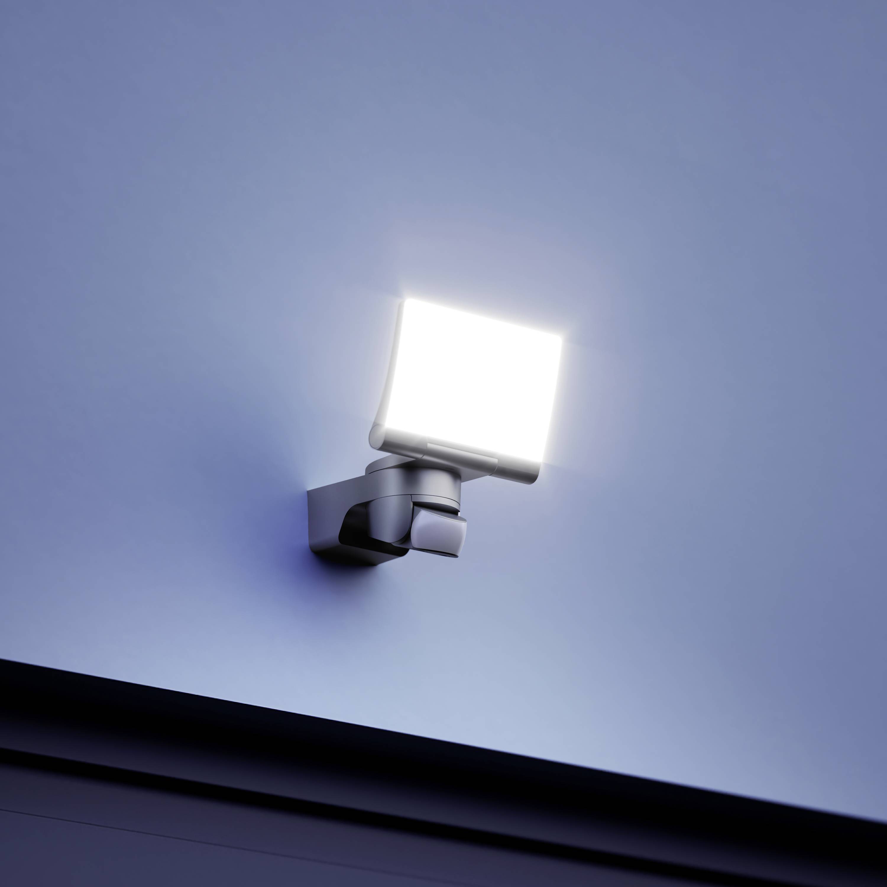 Ein weißer Scheinwerfer mit hellem Licht ist an einer grauen Wand montiert und leuchtet nach unten.