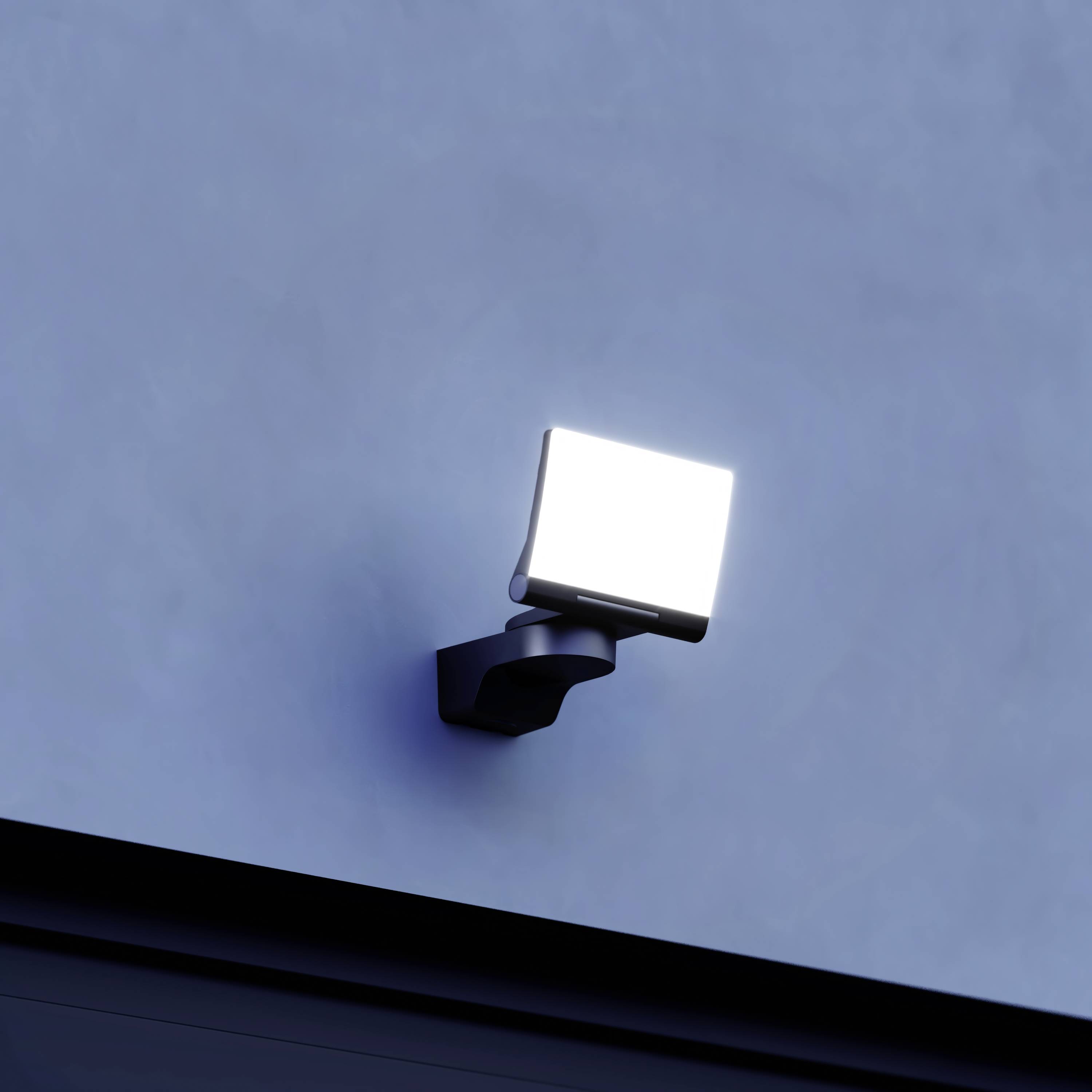 Eine helle Außenlampe ist an einer blauen Wand montiert und leuchtet stark.