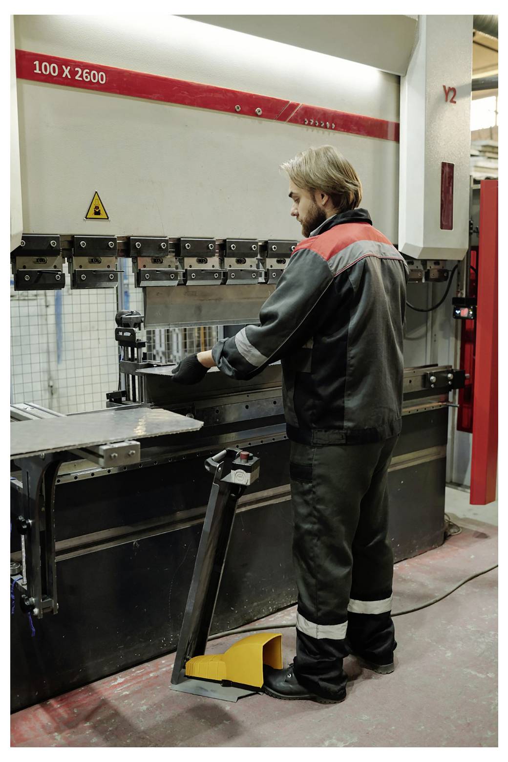 Fabrikarbeiter bedient eine große Industriepressenbremse, positioniert ein Metallblech zum Biegen in einer Werkstatt.