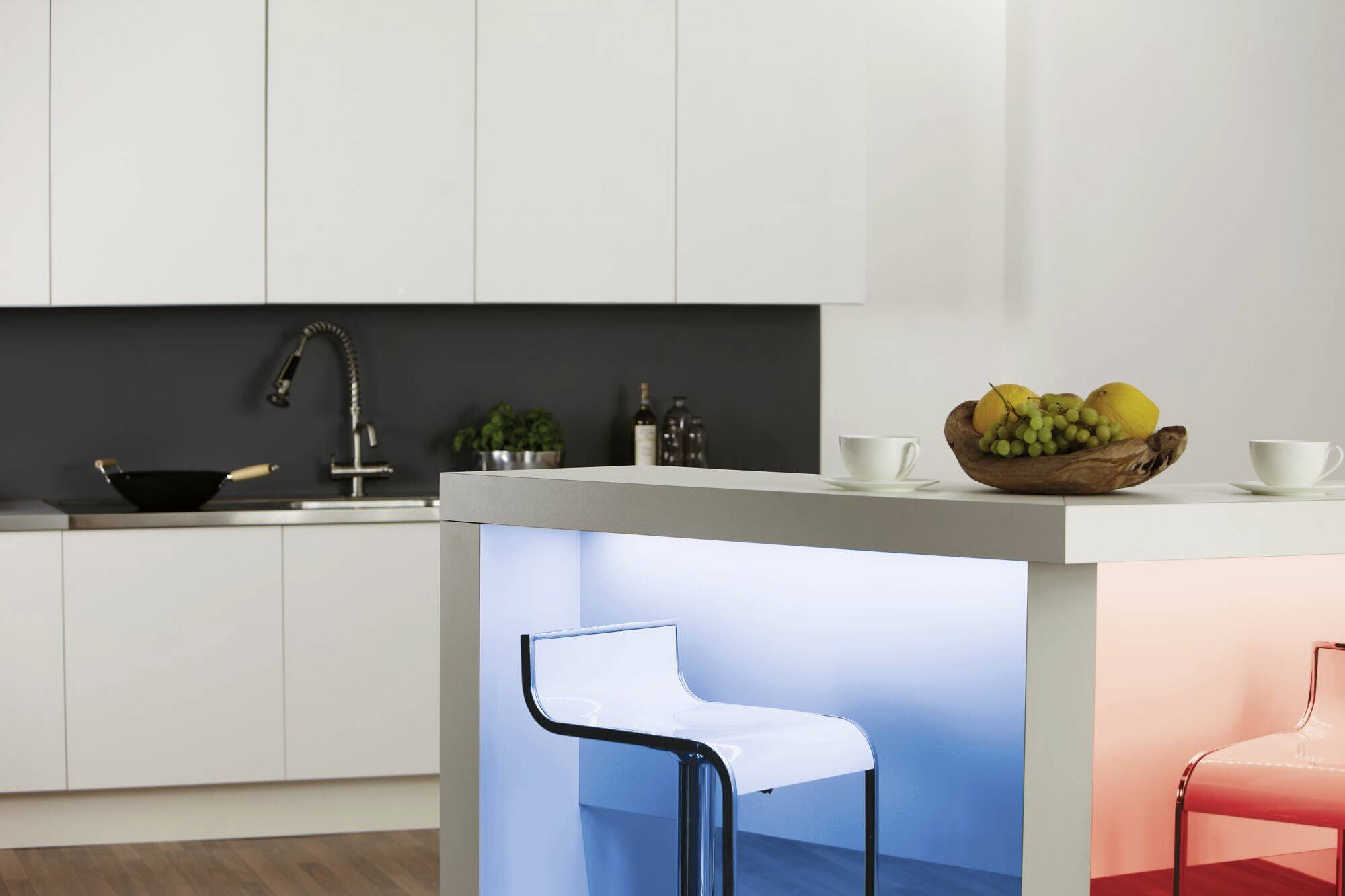Moderne Küche mit weißem Schrank, Obstschale auf der Theke und beleuchtetem Kühler. Zwei weiße Stühle stehen an der Insel.
