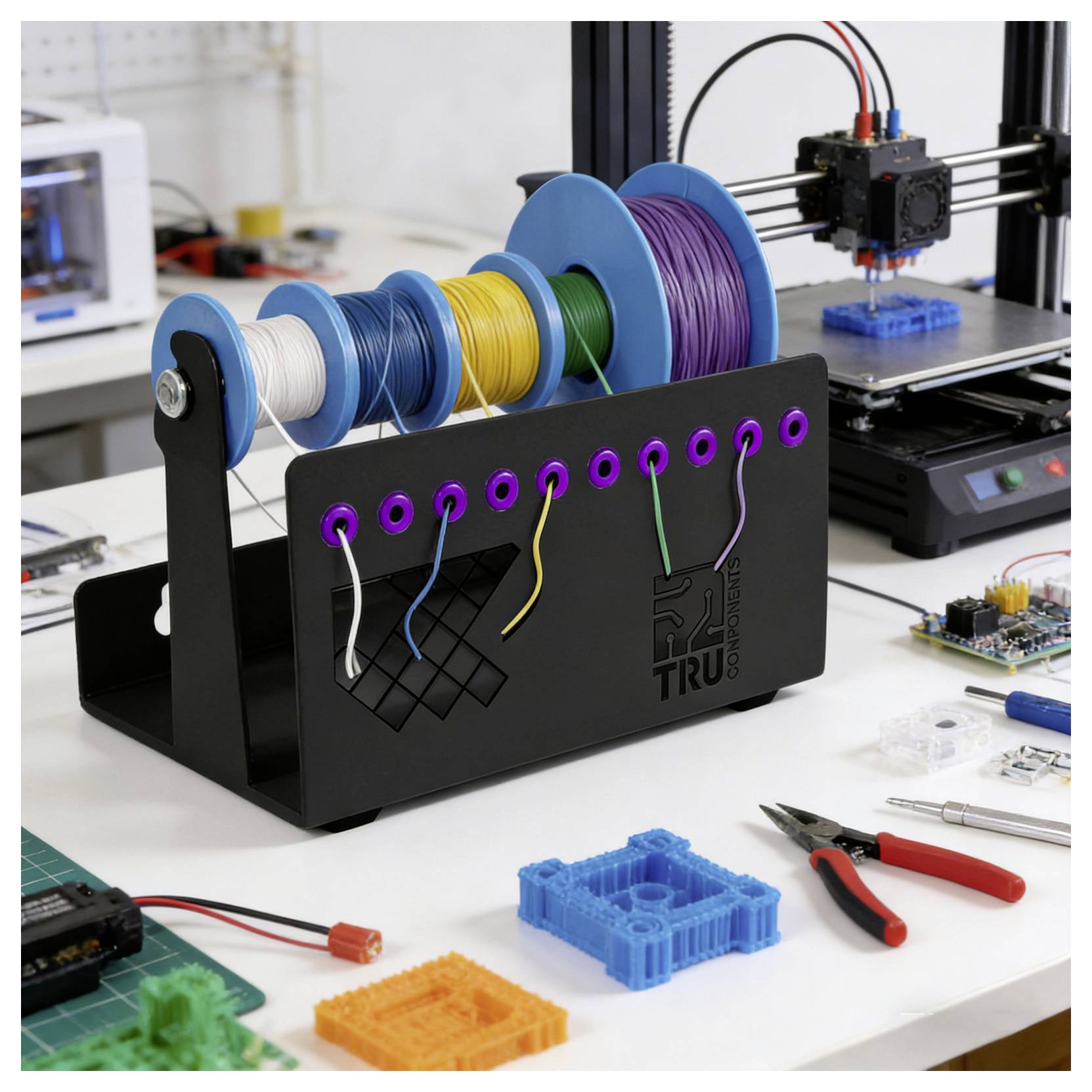 3D-Drucker-Filament-Organizer mit Spulen aus weißem, blauem, gelbem, grünem und violettem Filament; Kabel, die durch beschriftete Löcher auf einer Werkbank geleitet werden.