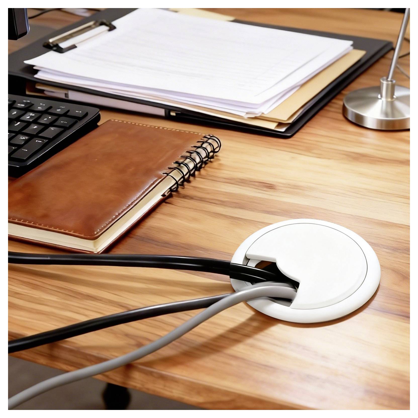 Ein hölzerner Schreibtisch mit einer schwarzen Tastatur, einem braunen Notizbuch und Dokumenten. Kabel ragen aus einer weißen Kabeldurchführung heraus.