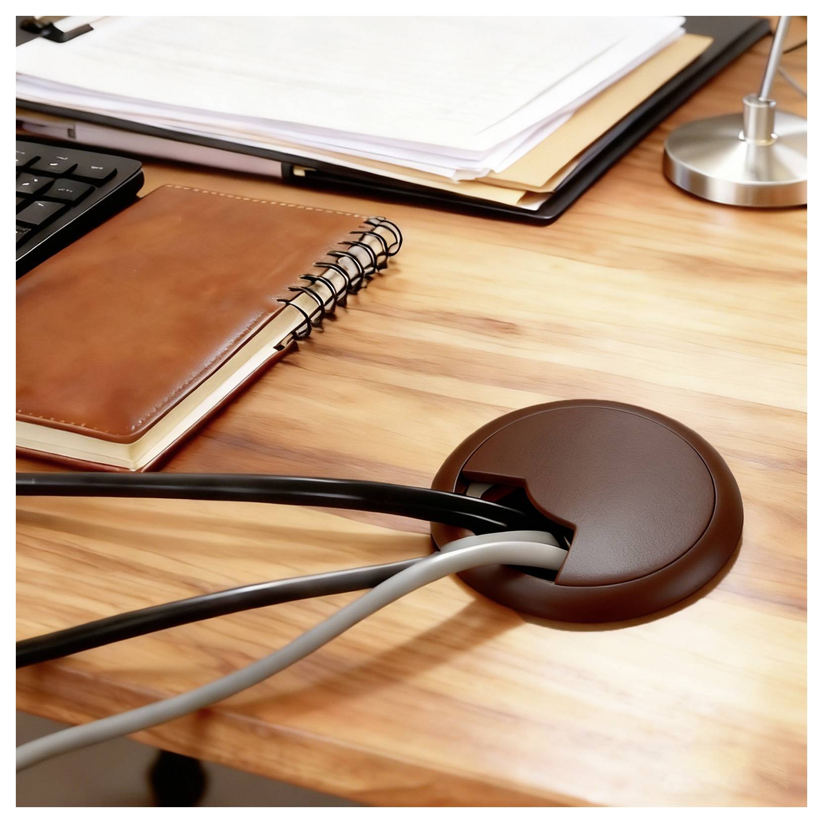 Ein aufgeräumter Schreibtisch mit einem Notizbuch, einer Tastatur und einem Kabelorganizer, der Kabel durch eine Öffnung leitet und so einen geordneten Arbeitsplatz schafft.