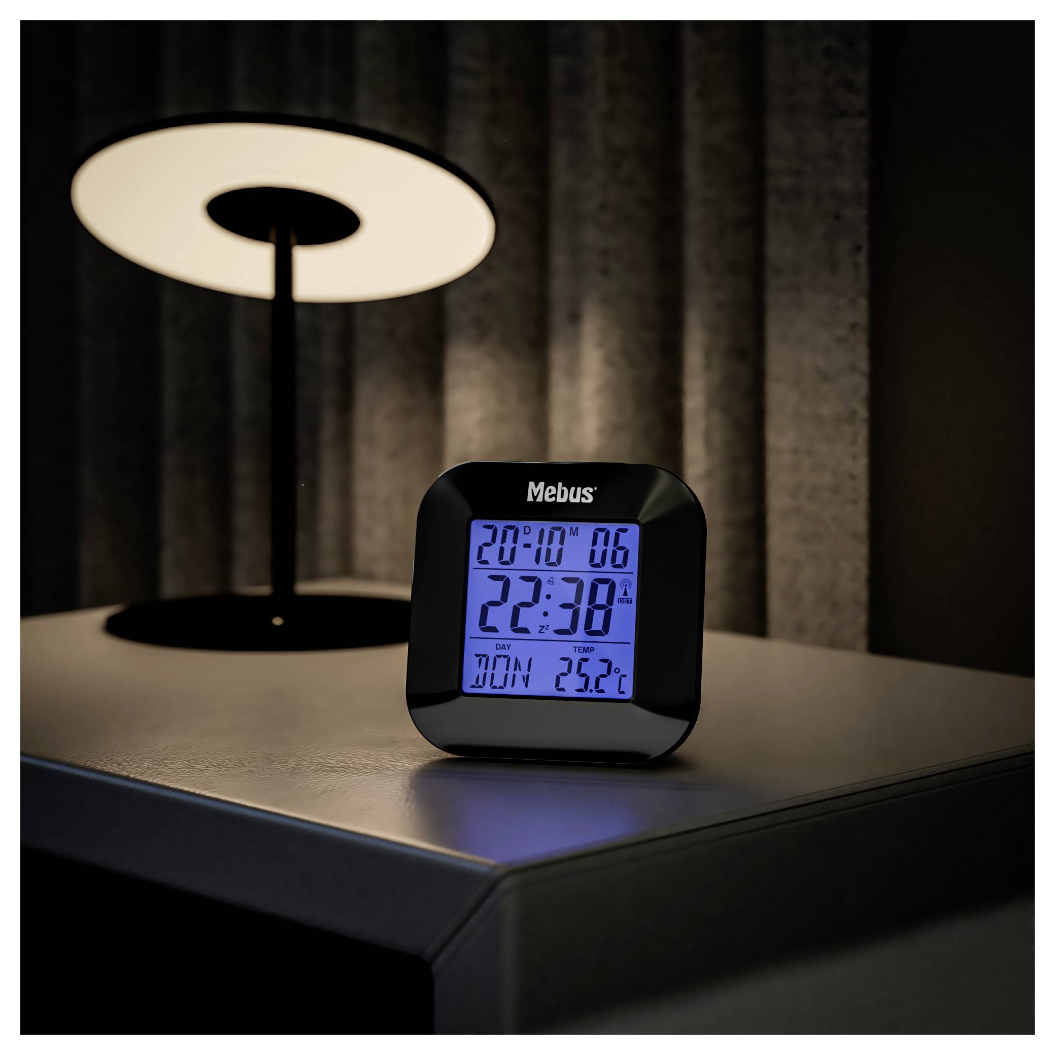 Eine digitale Uhr zeigt die Zeit 22:38 mit dem Datum 20.10 und eine Temperatur von 25°C an und steht auf einem schwach beleuchteten Tisch.